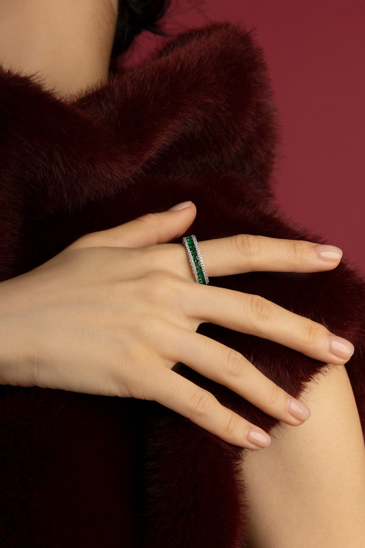 Woman wearing APM ring, emerald green brilliance wrapped in quiet winter elegance.