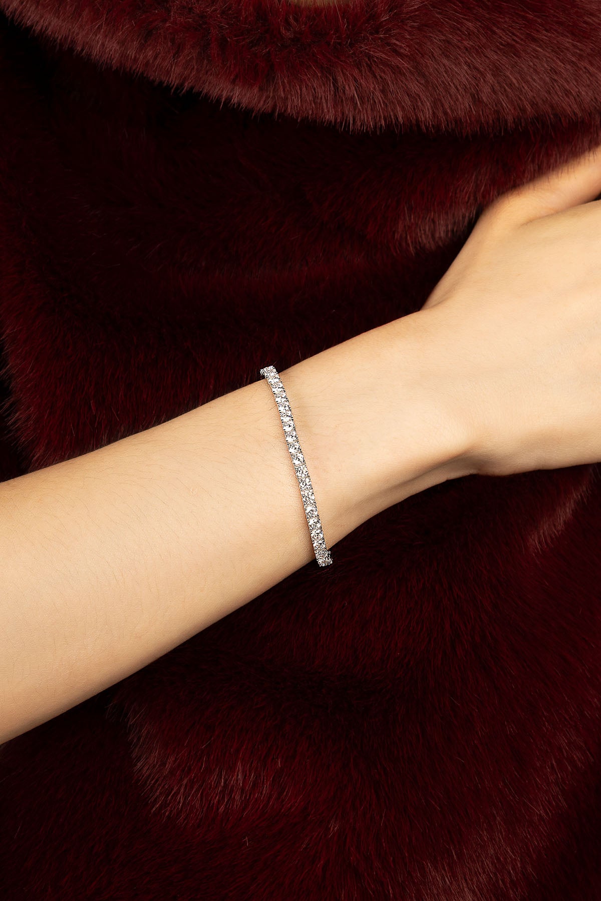 Woman wearing APM Monaco tennis bracelet, a luminous whisper against burgundy elegance.