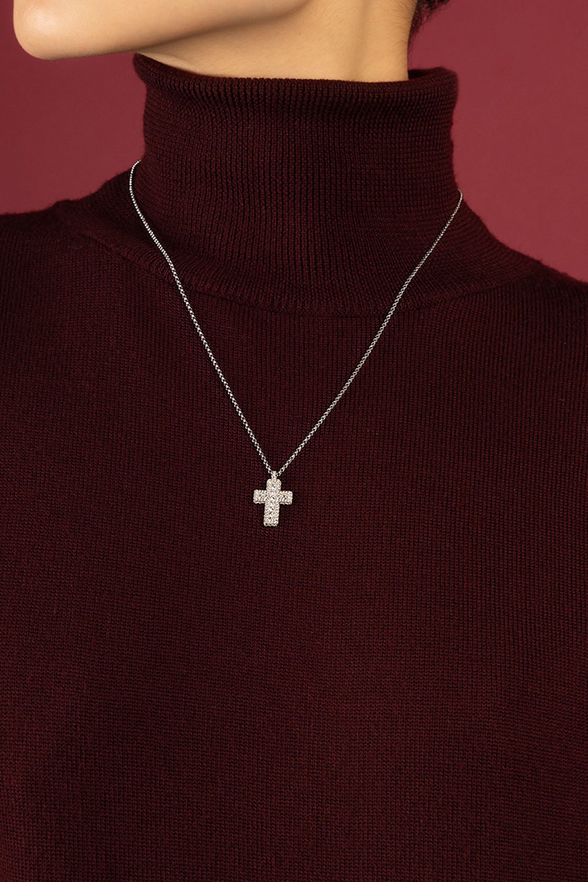 Woman wearing APM cross necklace, quiet elegance against rich burgundy.