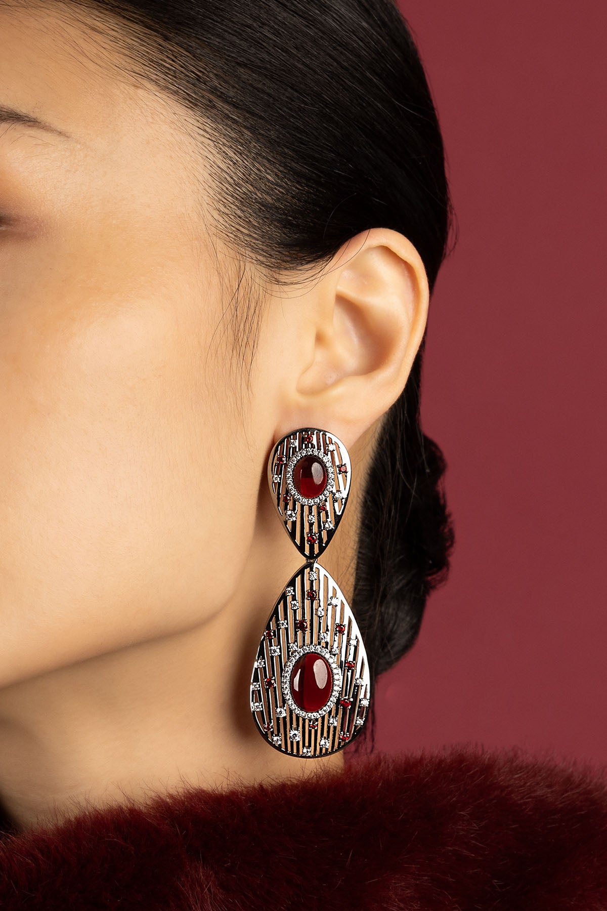 Woman wearing APM statement earrings, deep red allure with bold cinematic elegance.