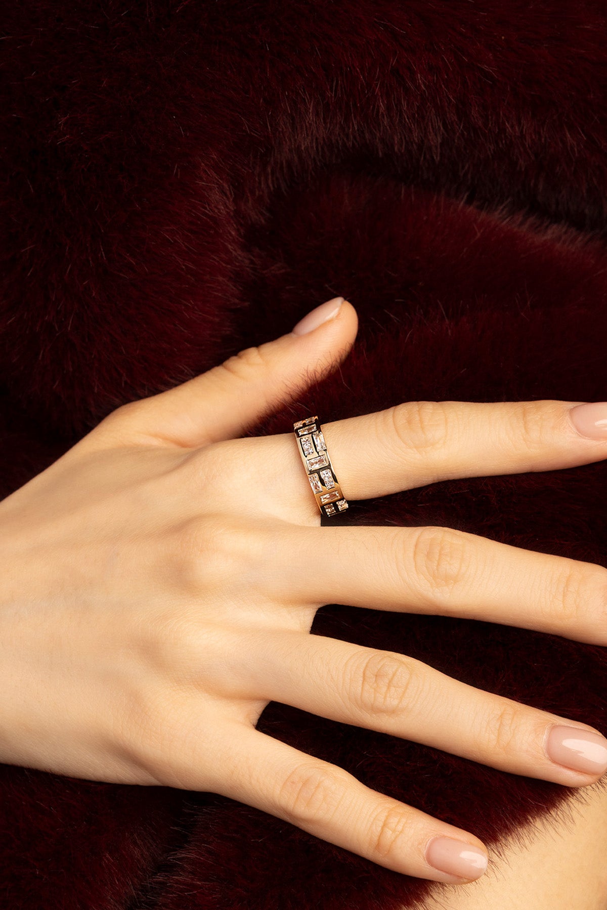 Woman wearing APM ring, a golden whisper of quiet luxury against plush burgundy.