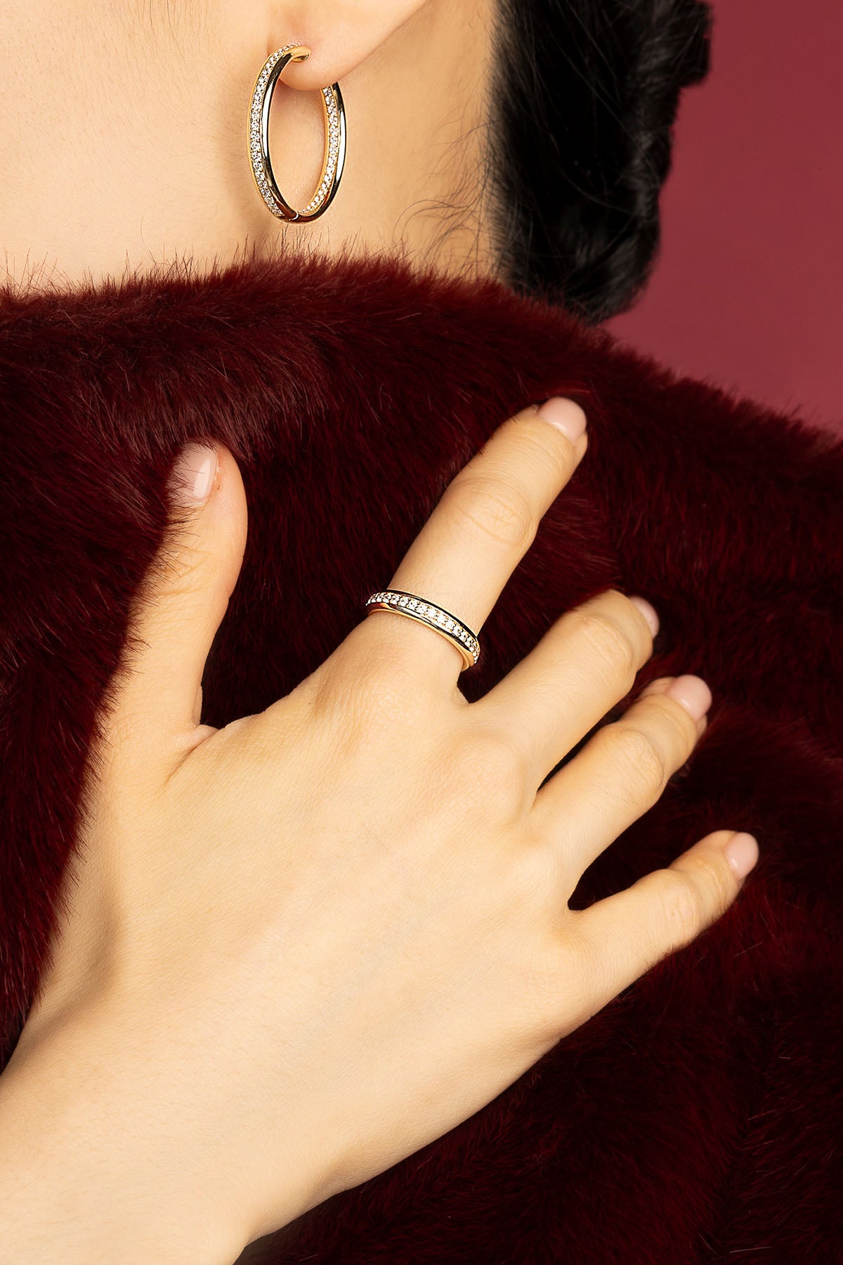 Woman wearing APM hoop earrings and ring, a golden glow against burgundy elegance.