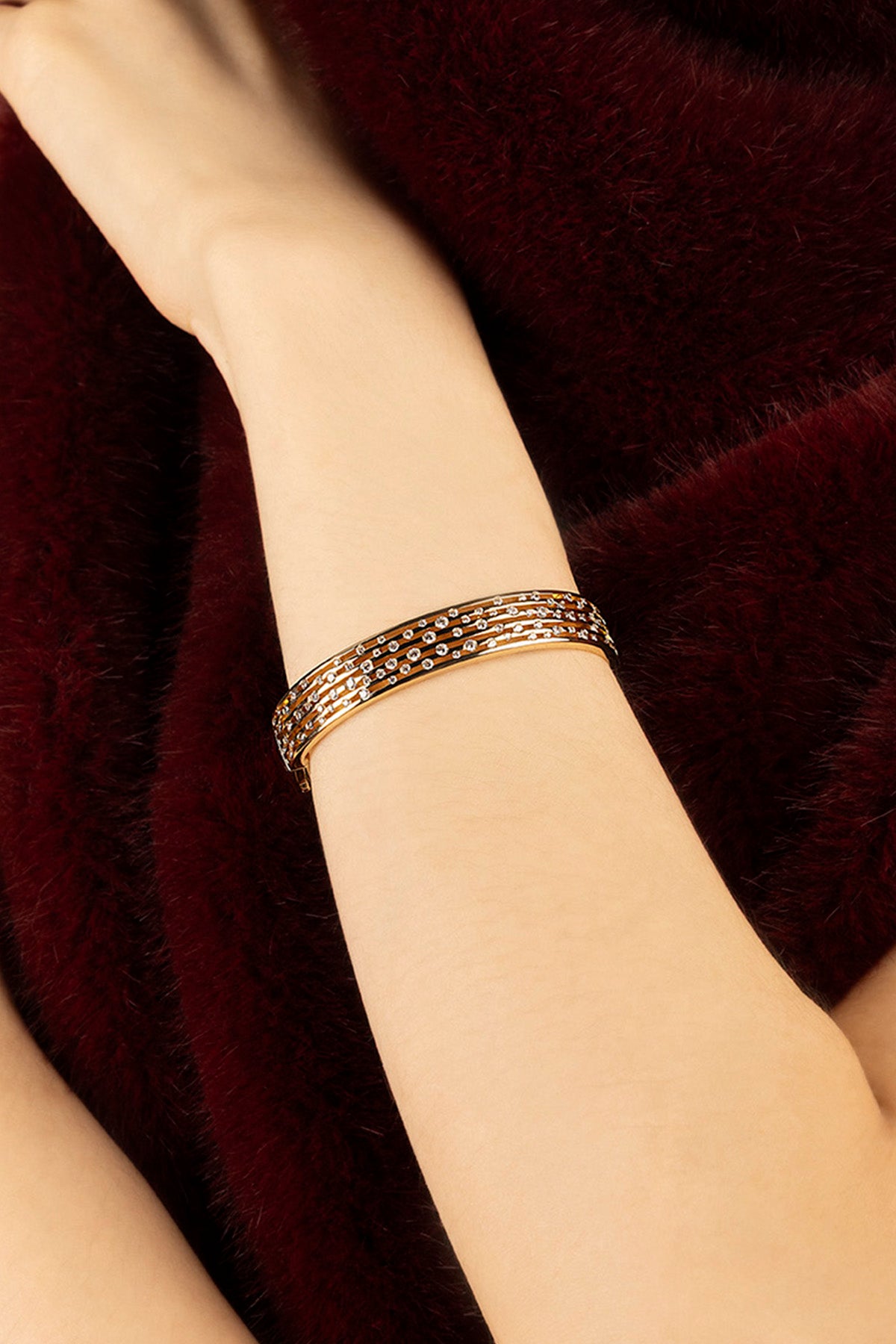Woman wearing APM Monaco bracelet, a shimmering wrist statement against velvety burgundy.