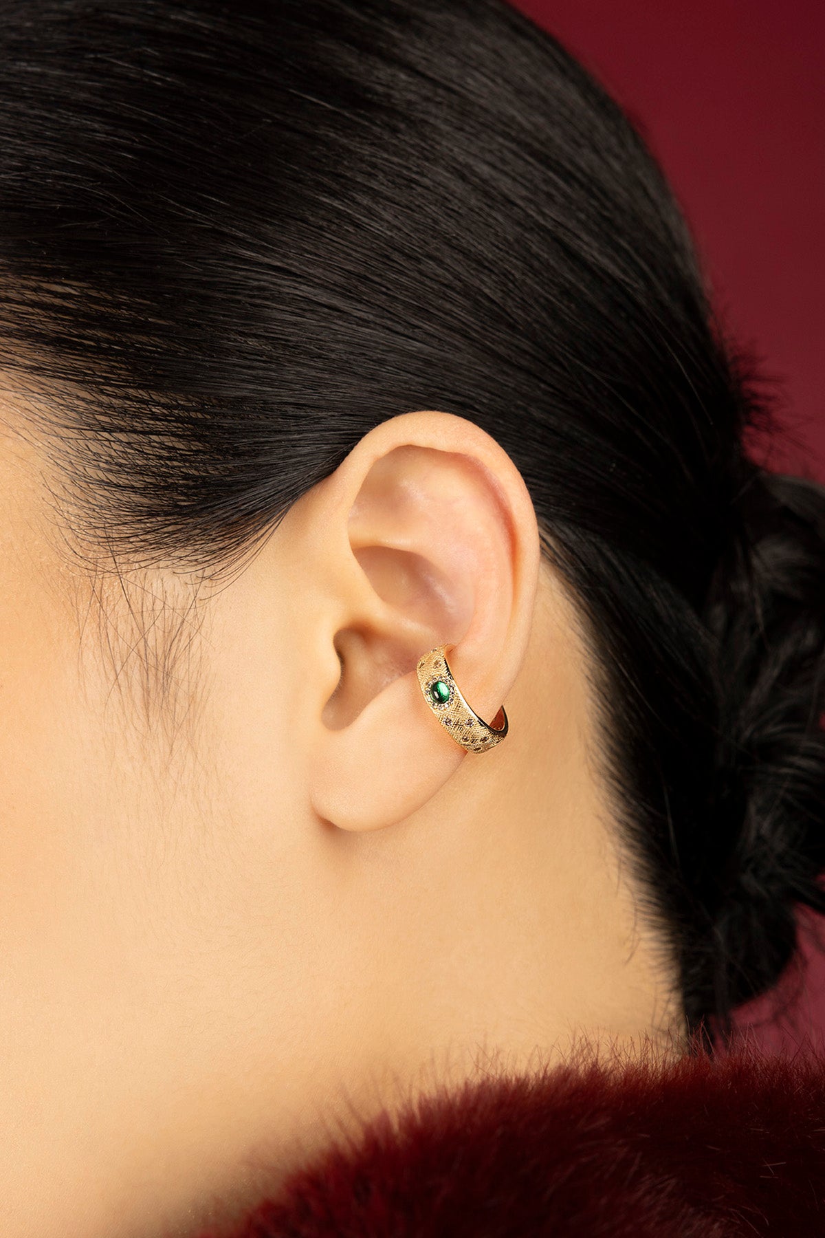 Woman wearing APM ear cuff, a golden whisper with an emerald green glow.