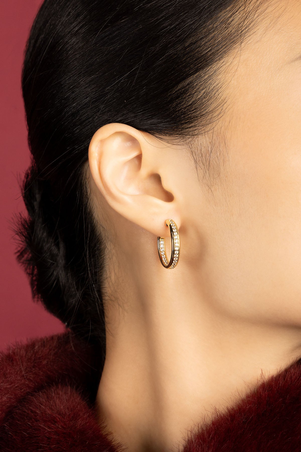 Woman wearing APM hoop earrings, a golden shimmer against crimson elegance.