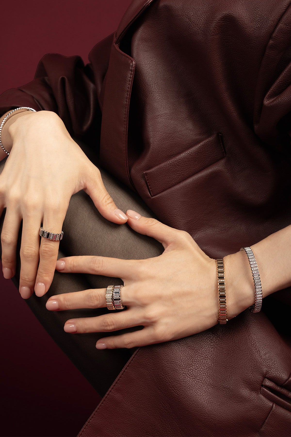 Woman wearing APM Monaco rings and bracelets, a luminous statement against rich burgundy leather.
