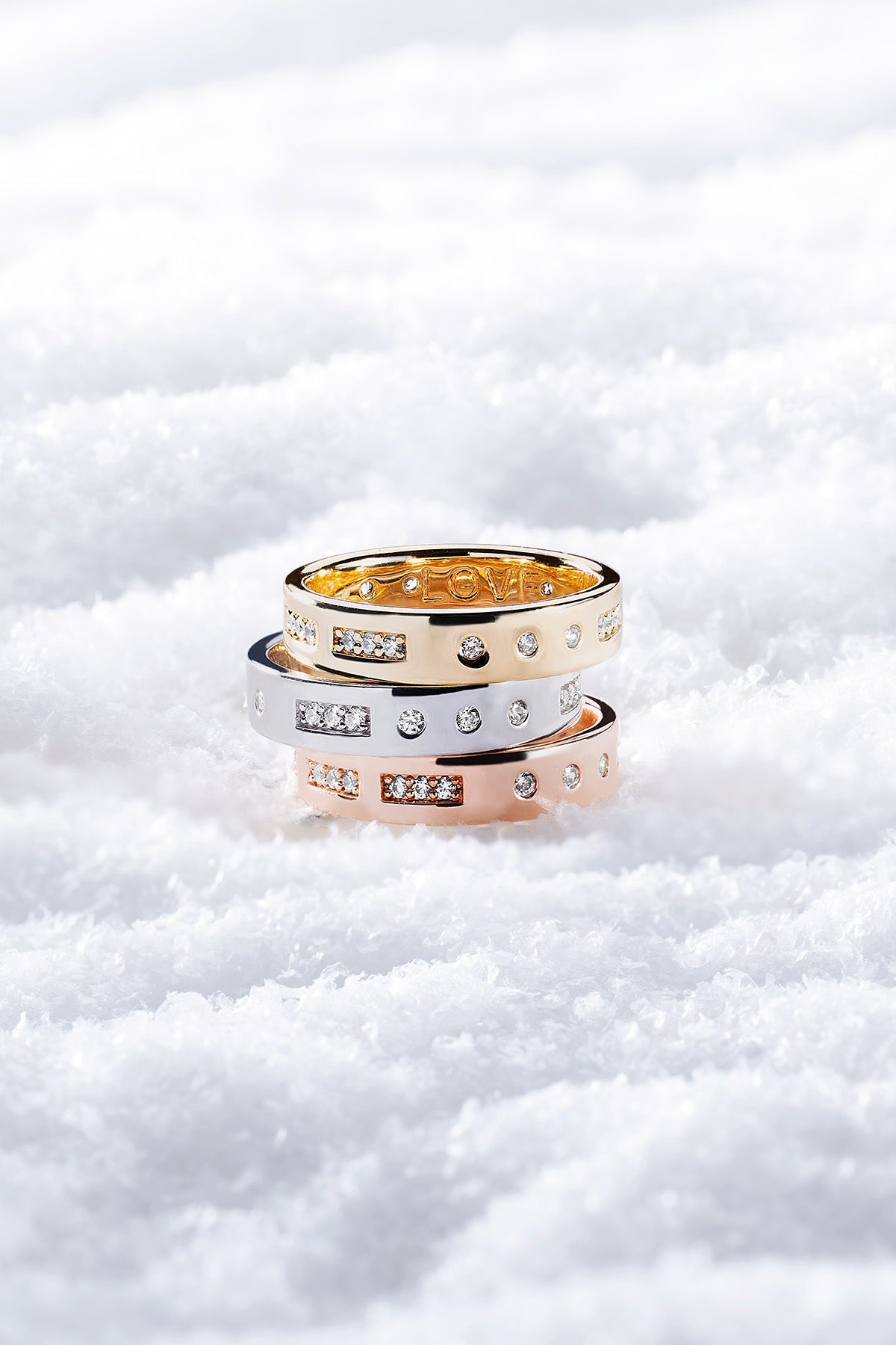 Three APM MONACO gold and rose gold rings stacked on a snowy background