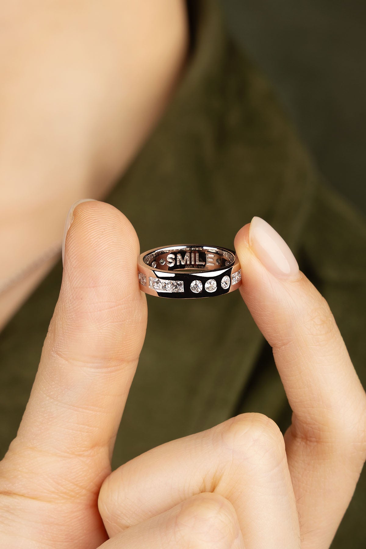 Person holding a silver ring with 'SMILE' engraving on a blurred background