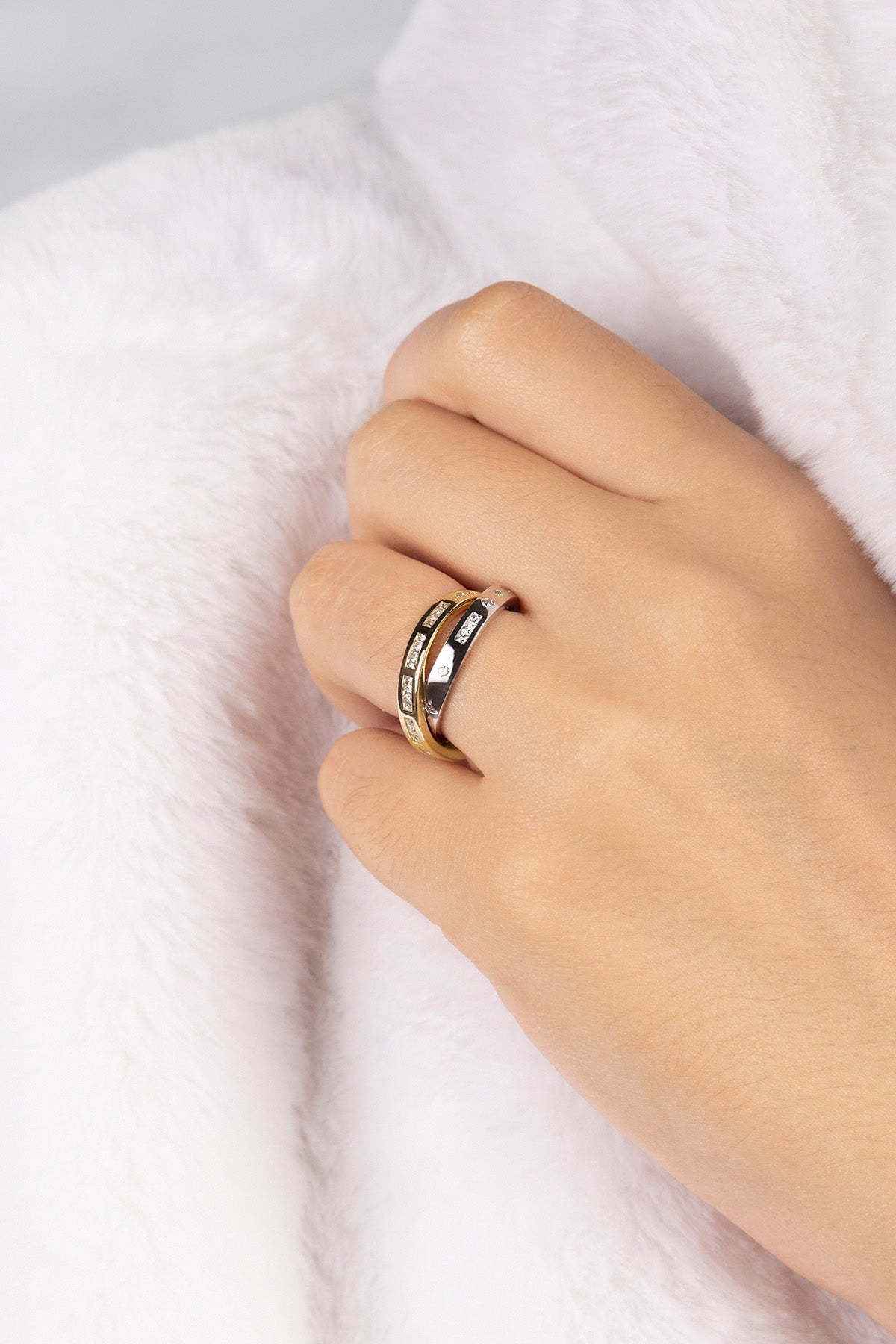 Hand wearing a gold and Silver-tone ring on a white fabric background