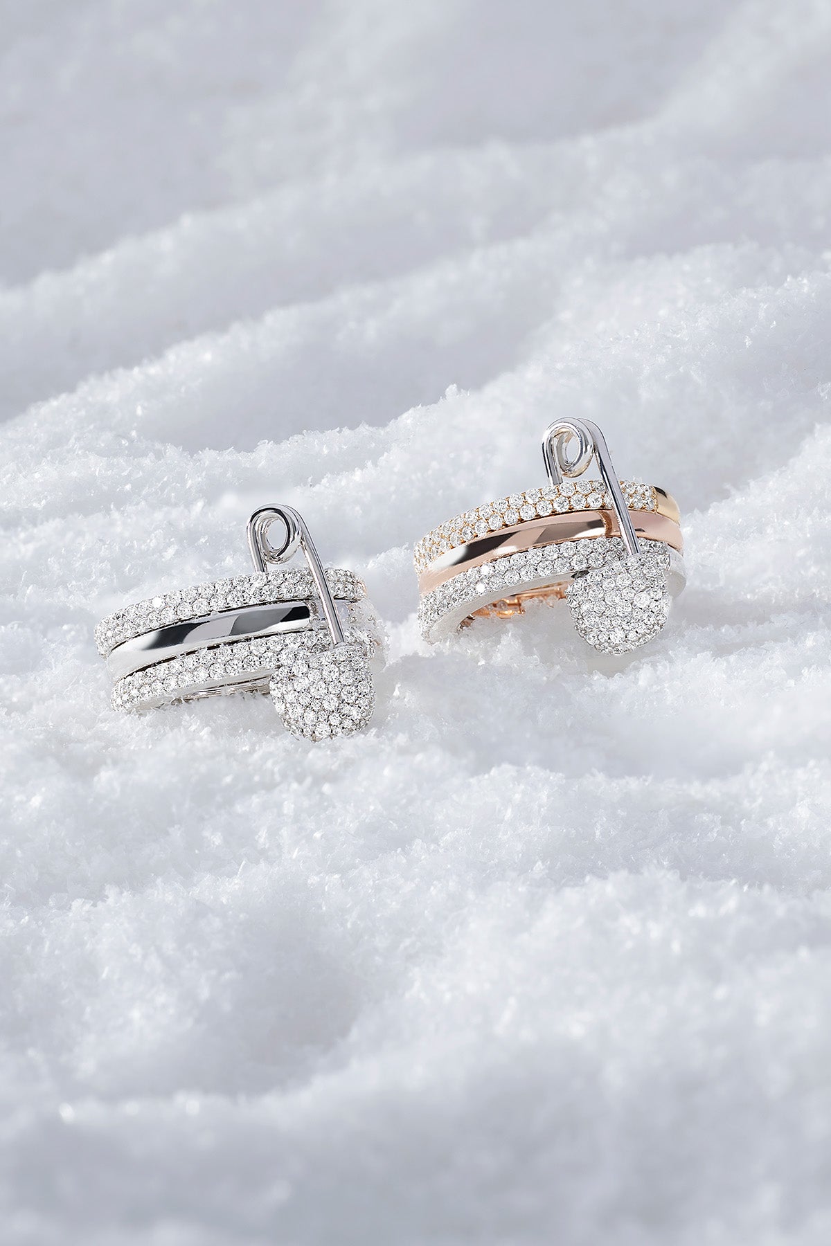 Two rings, one silver and one rose gold, with triple hoop and safety pin design from APM MONACO on a snowy background