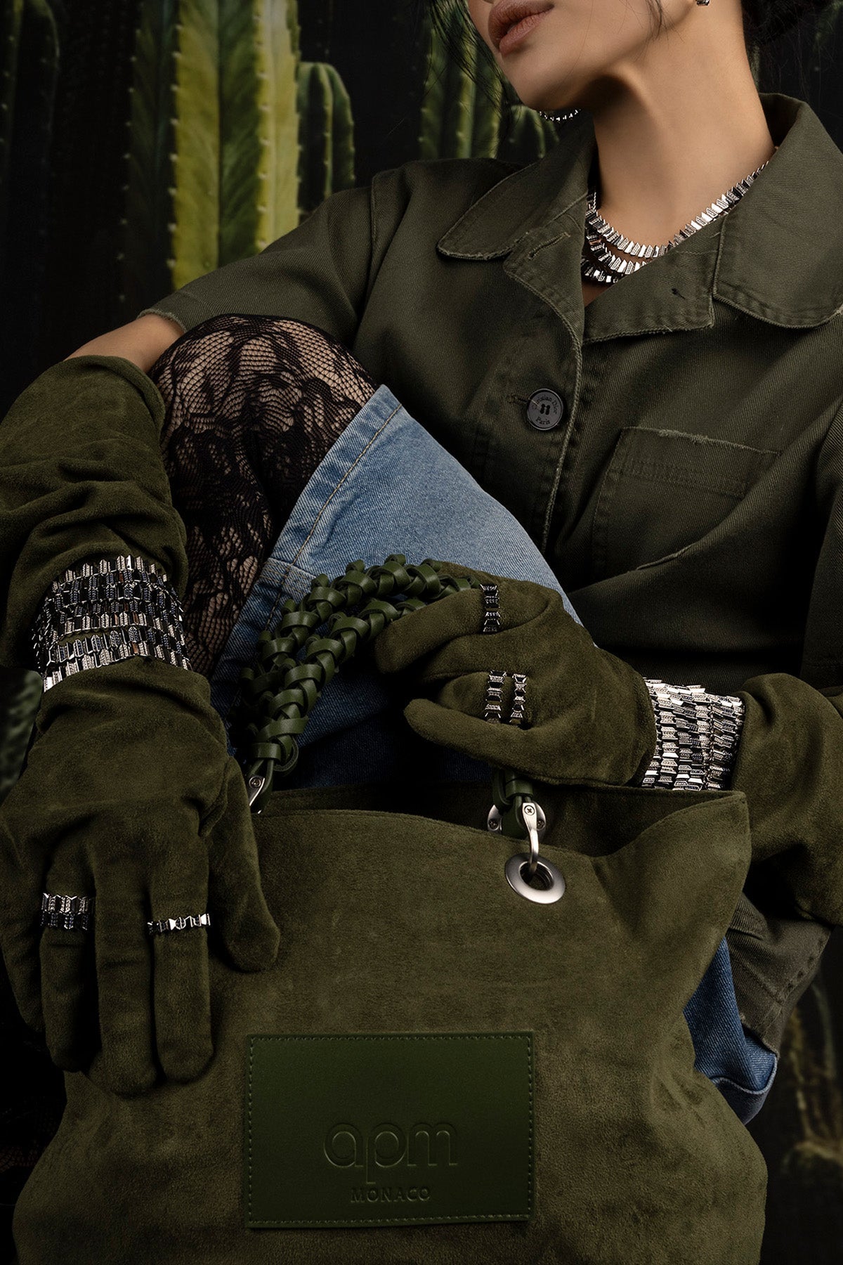 Person wearing green gloves, coat and jewelry with a cactus plant in the background