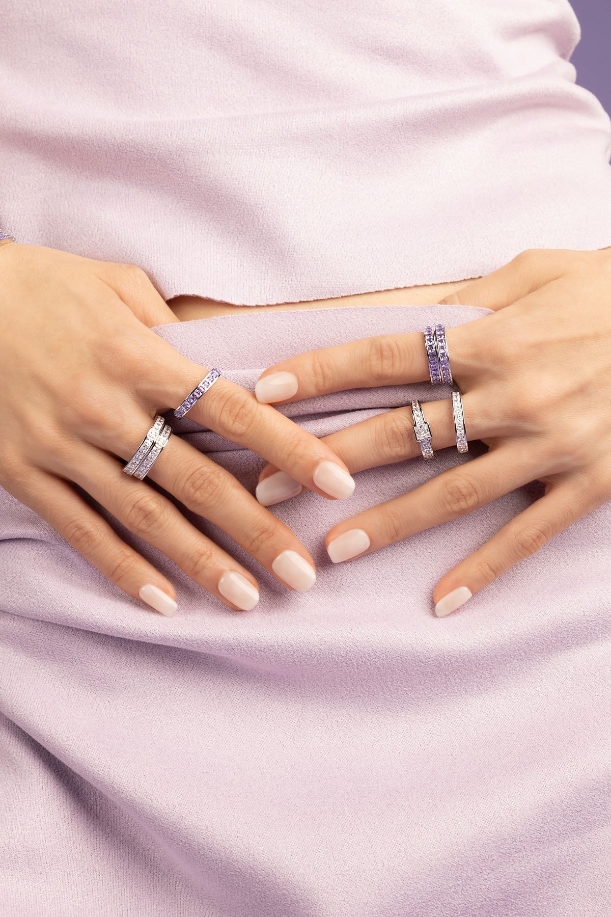Hand wearing a ring with purple zirconia stones against a light purple background