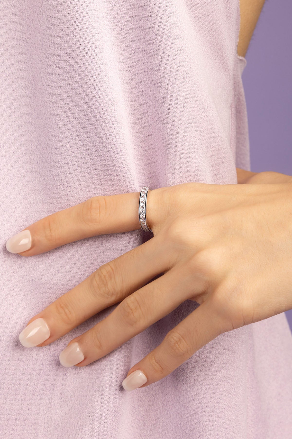 Hand wearing a white zirconia ring on a light purple background