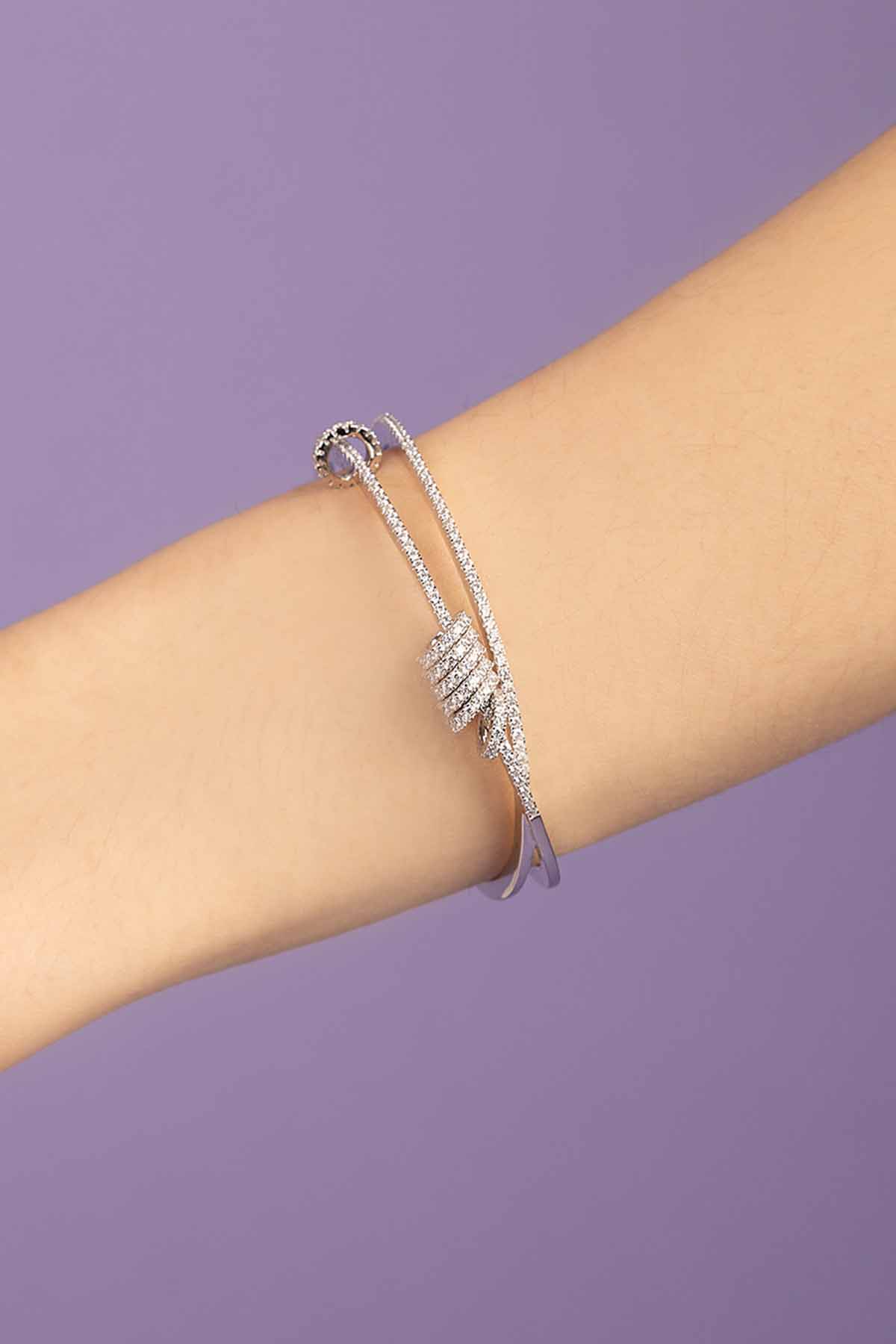 APM MONACO Silver cuff with sliding rings on a person's wrist against a purple background