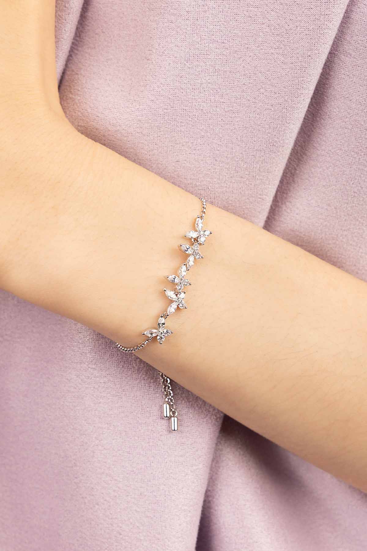 Silver butterfly bracelet on a person's wrist against a pink fabric background