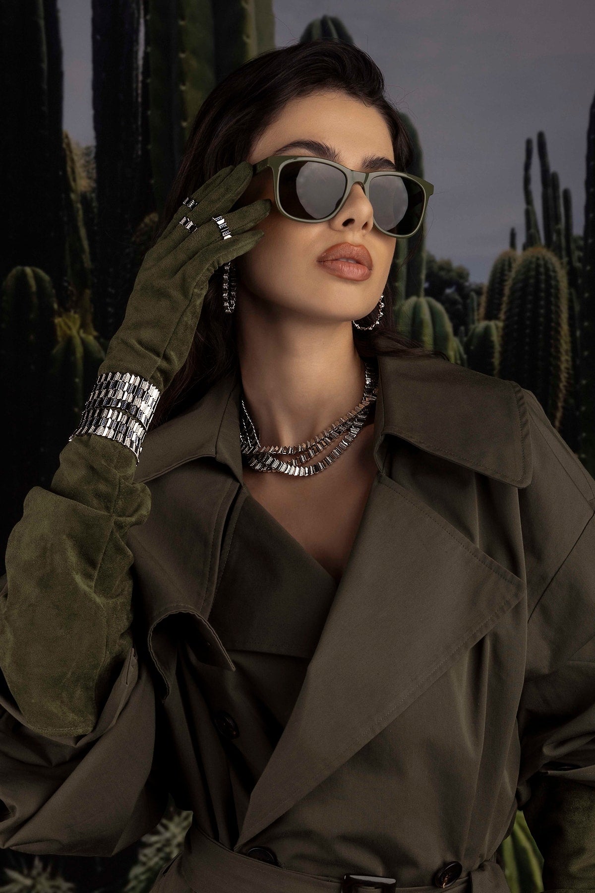Model in a trench coat and sunglasses with cacti in the background