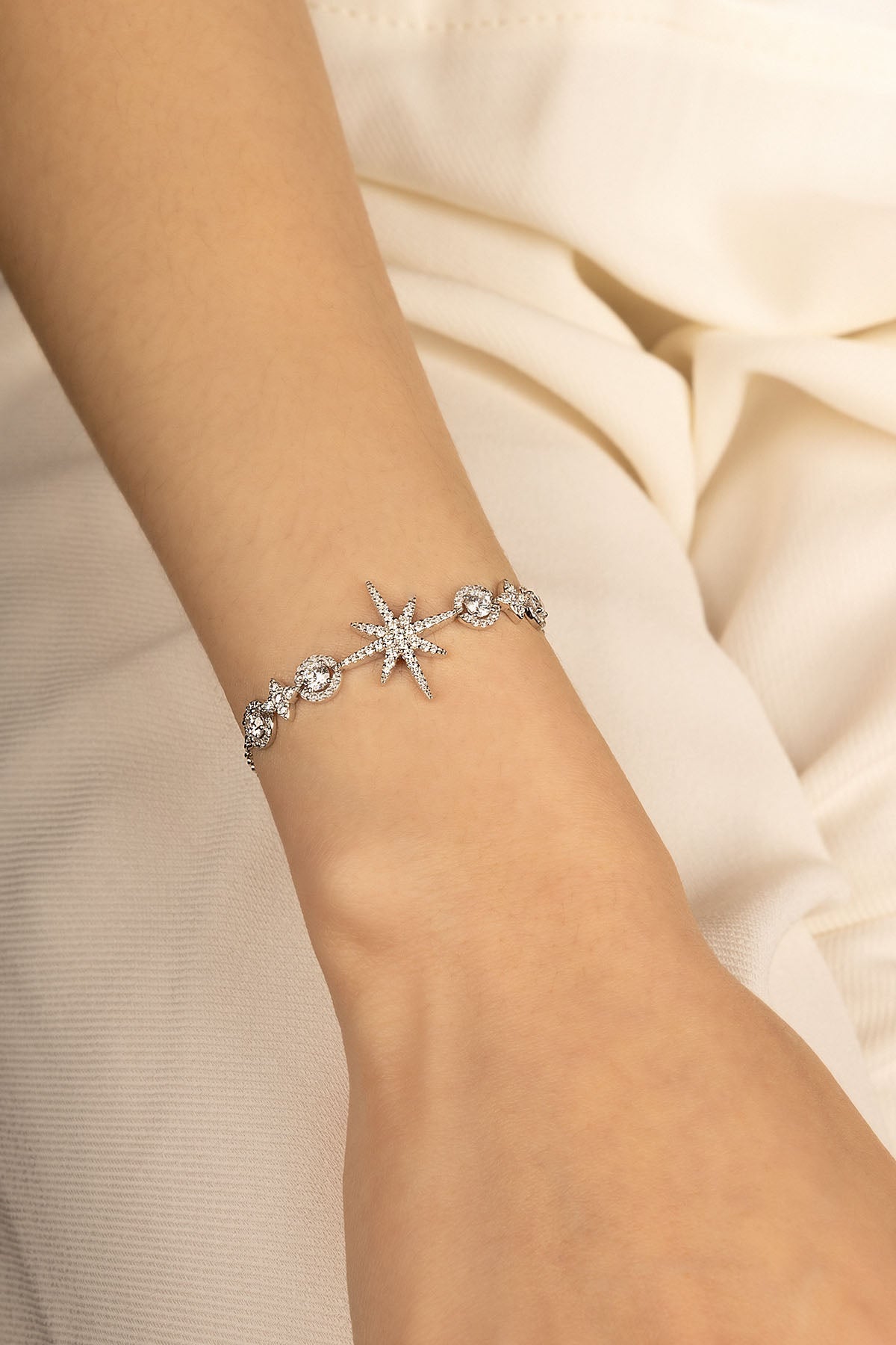 Silver bracelet with star design on a wrist against a soft beige background