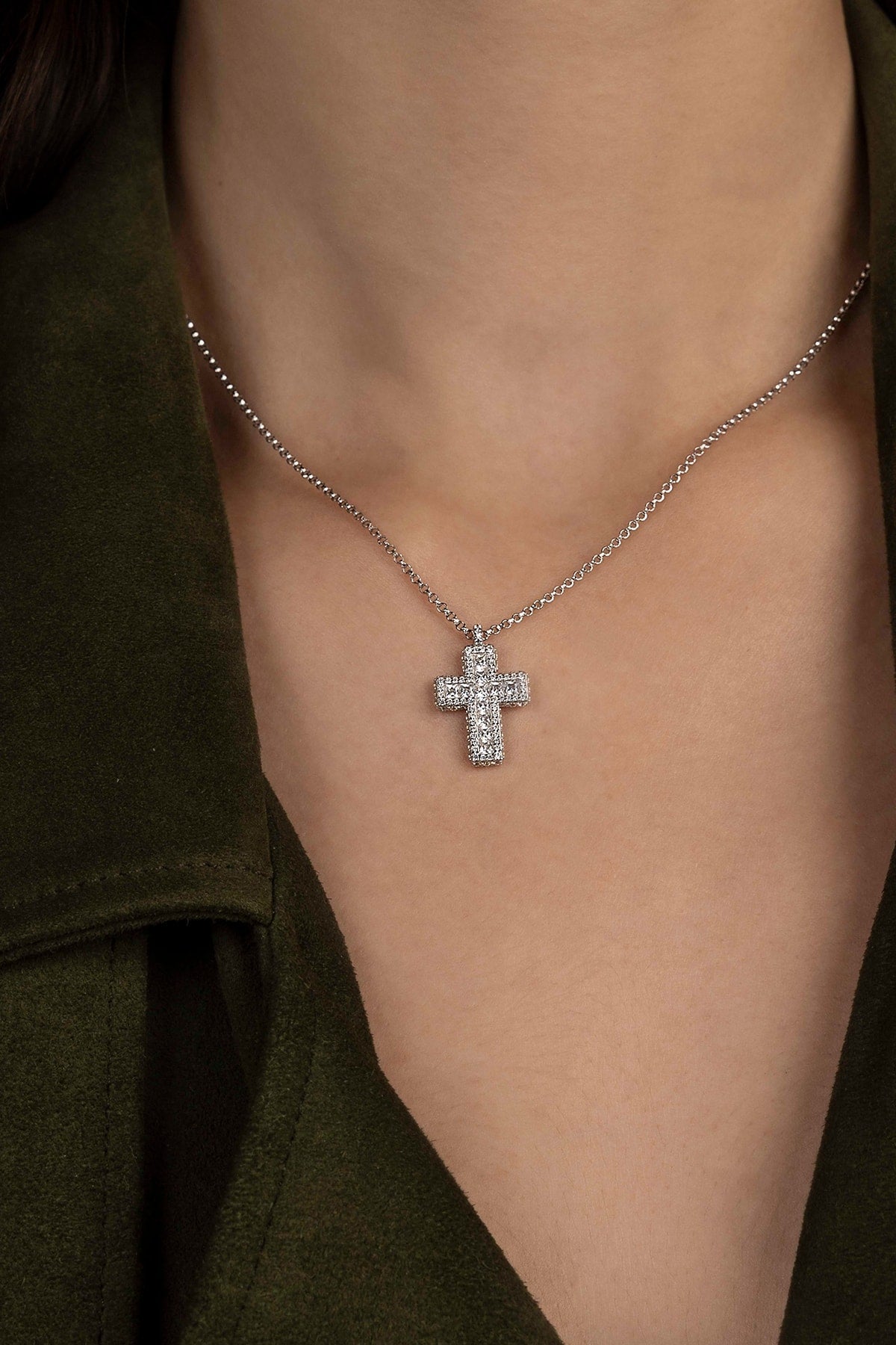 Silver cross necklace on a model's neck against a dark background