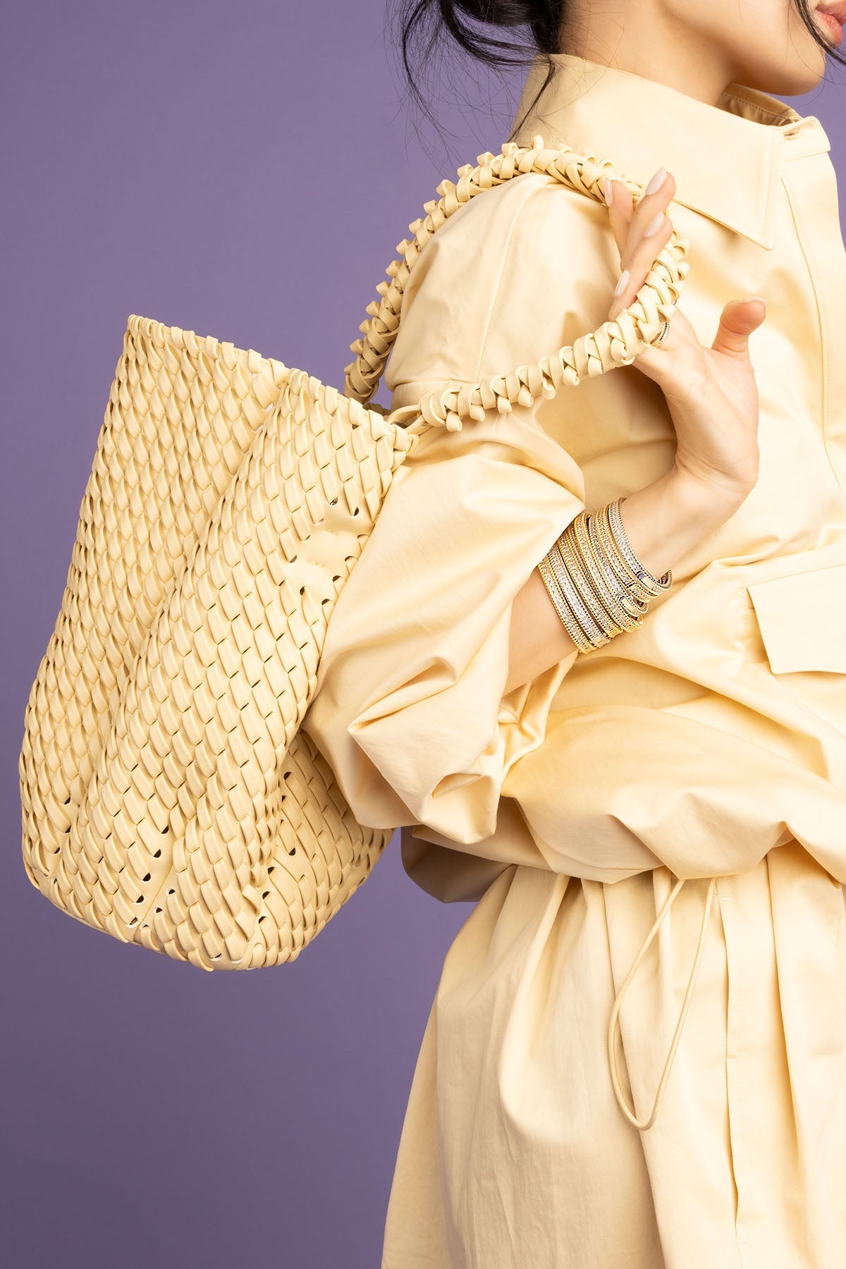 Person holding a woven handbag against a purple background