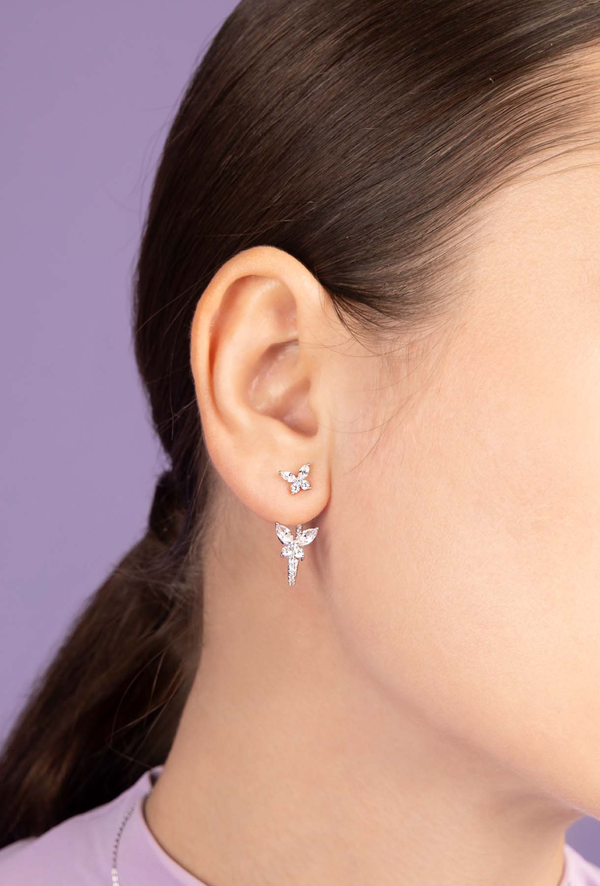 Close-up of a person wearing a silver earring with a purple background