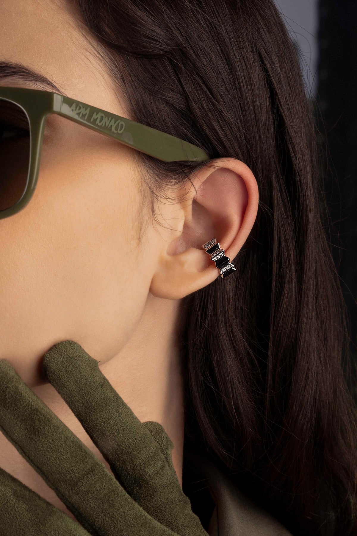 Close-up of a model wearing green sunglasses with a focus on an ear cuff