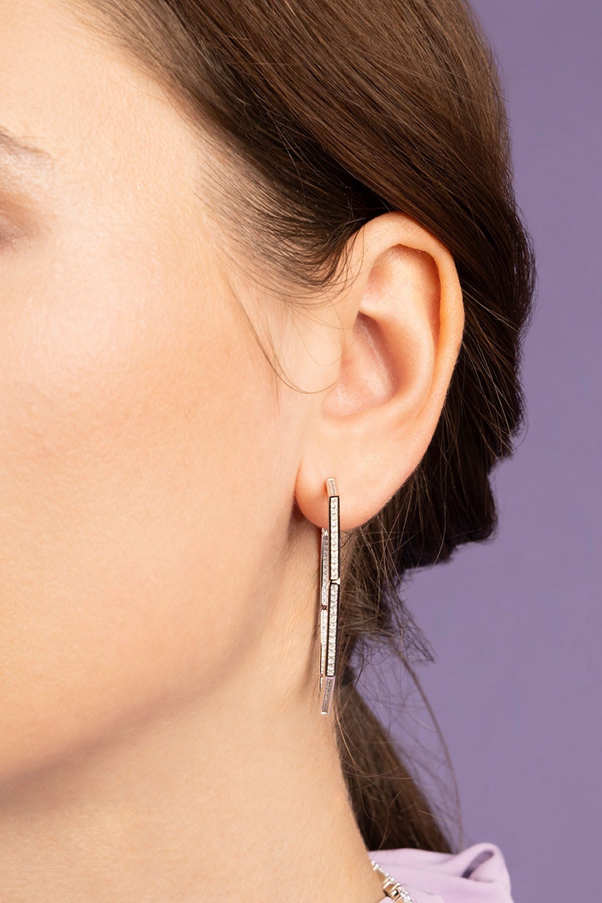Close-up of an ear wearing a silver earring with a purple background