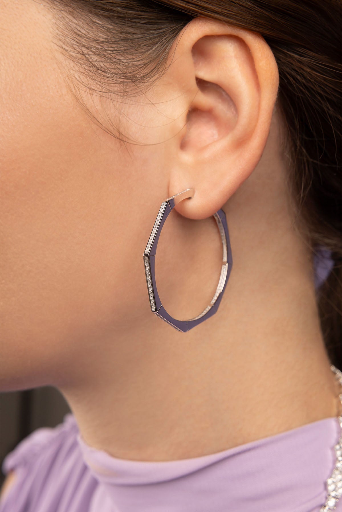 Close-up of an ear wearing a silver hoop earring with a purple background