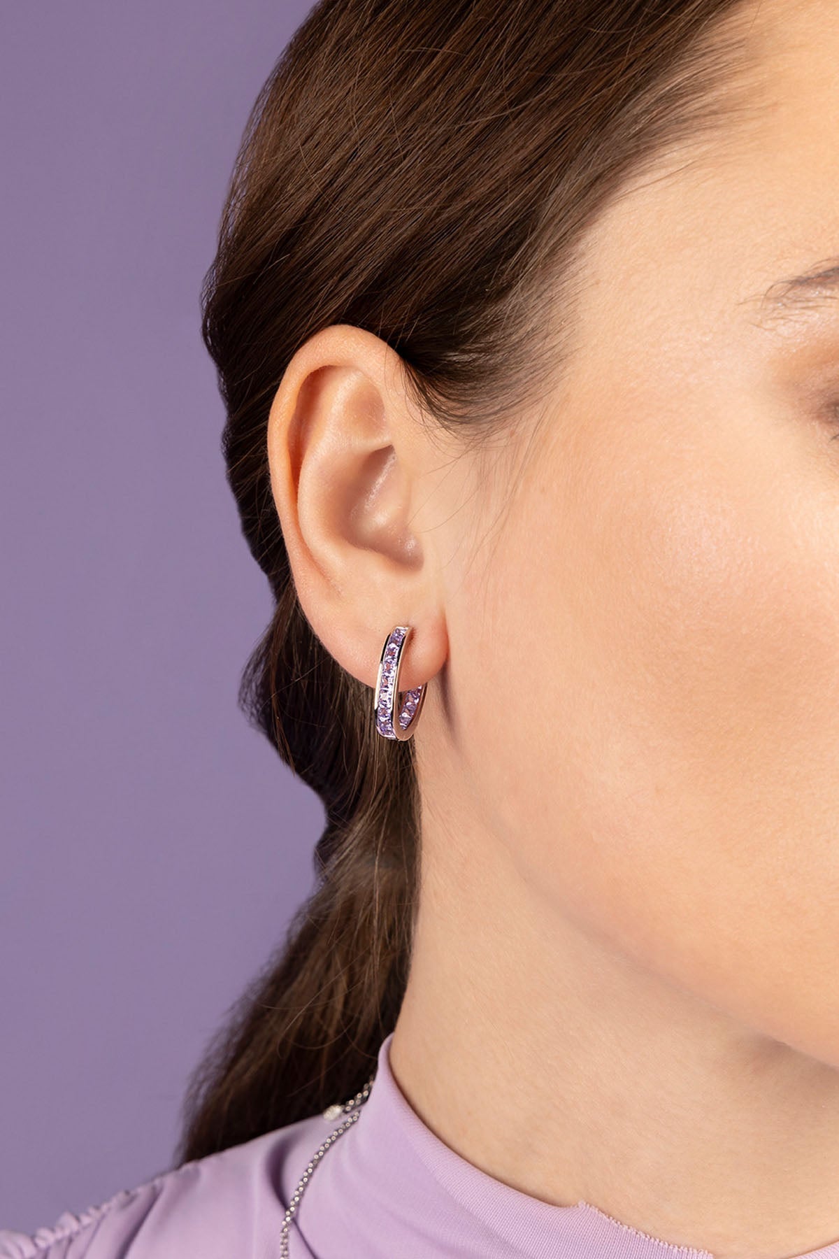 Close-up of a person wearing a silver hoop earring against a purple background
