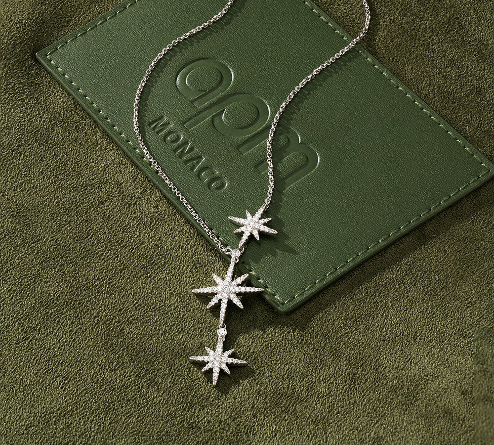 APM MONACO triple star-shaped Meteorites necklace on a green textured surface with 'APM MONACO' branding.