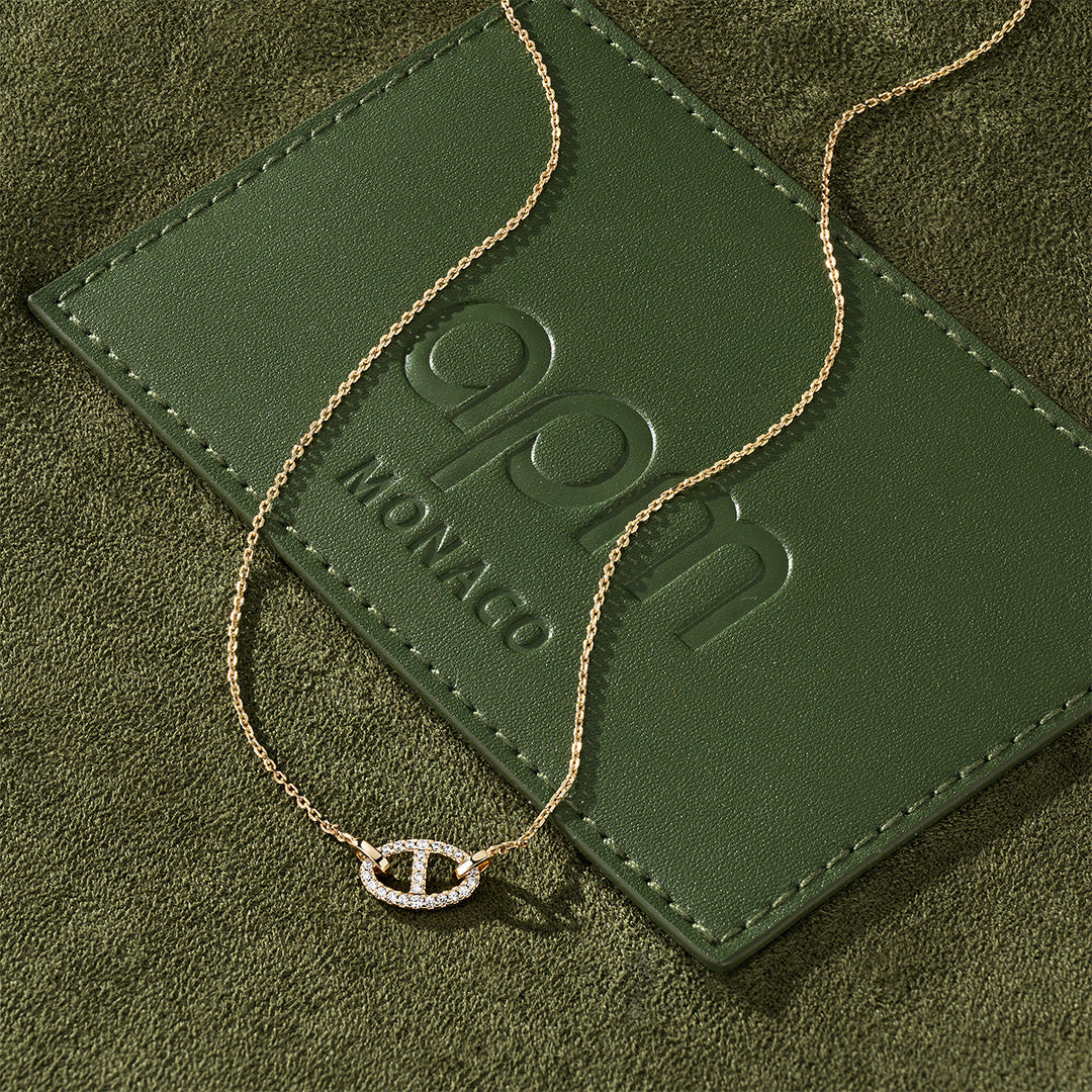 APM MONACO yacht club gold necklace  on a green textured surface
