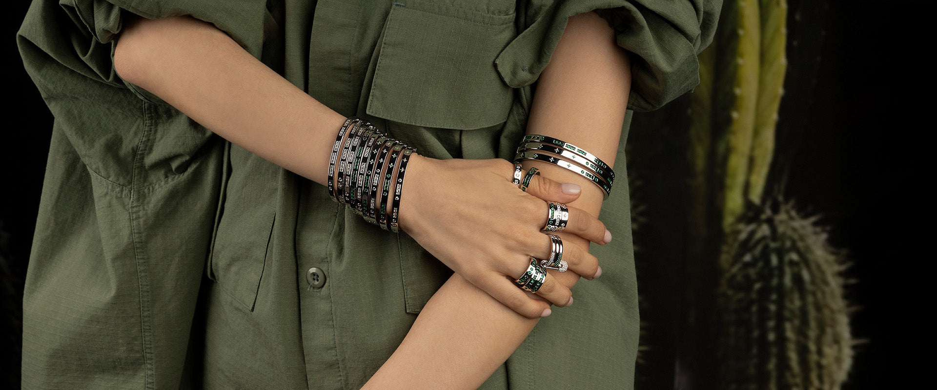 Person wearing multiple APM MONACO morse code  bracelets and rings on a dark green background