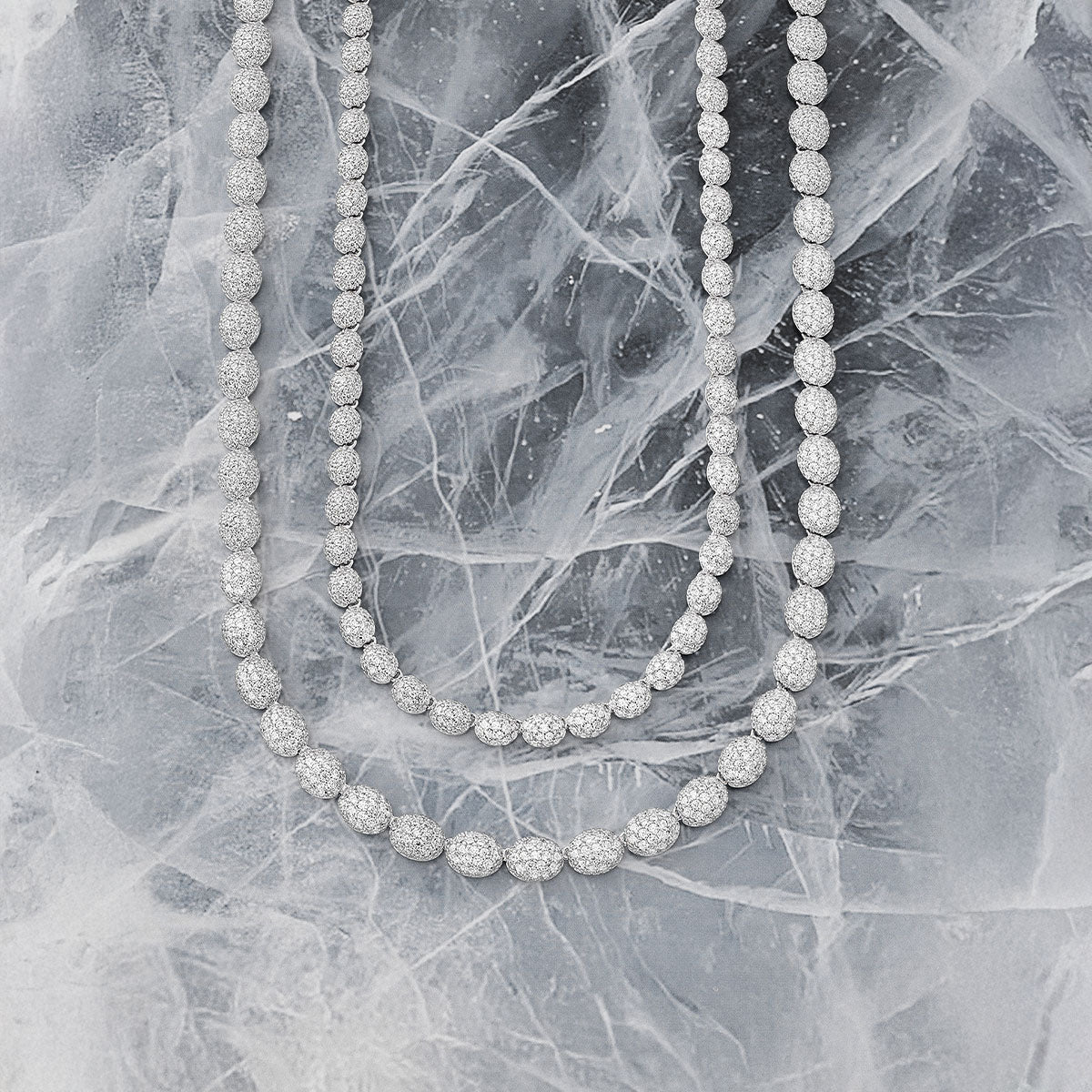 Two silver necklaces from APM MONACO, on a textured gray surface