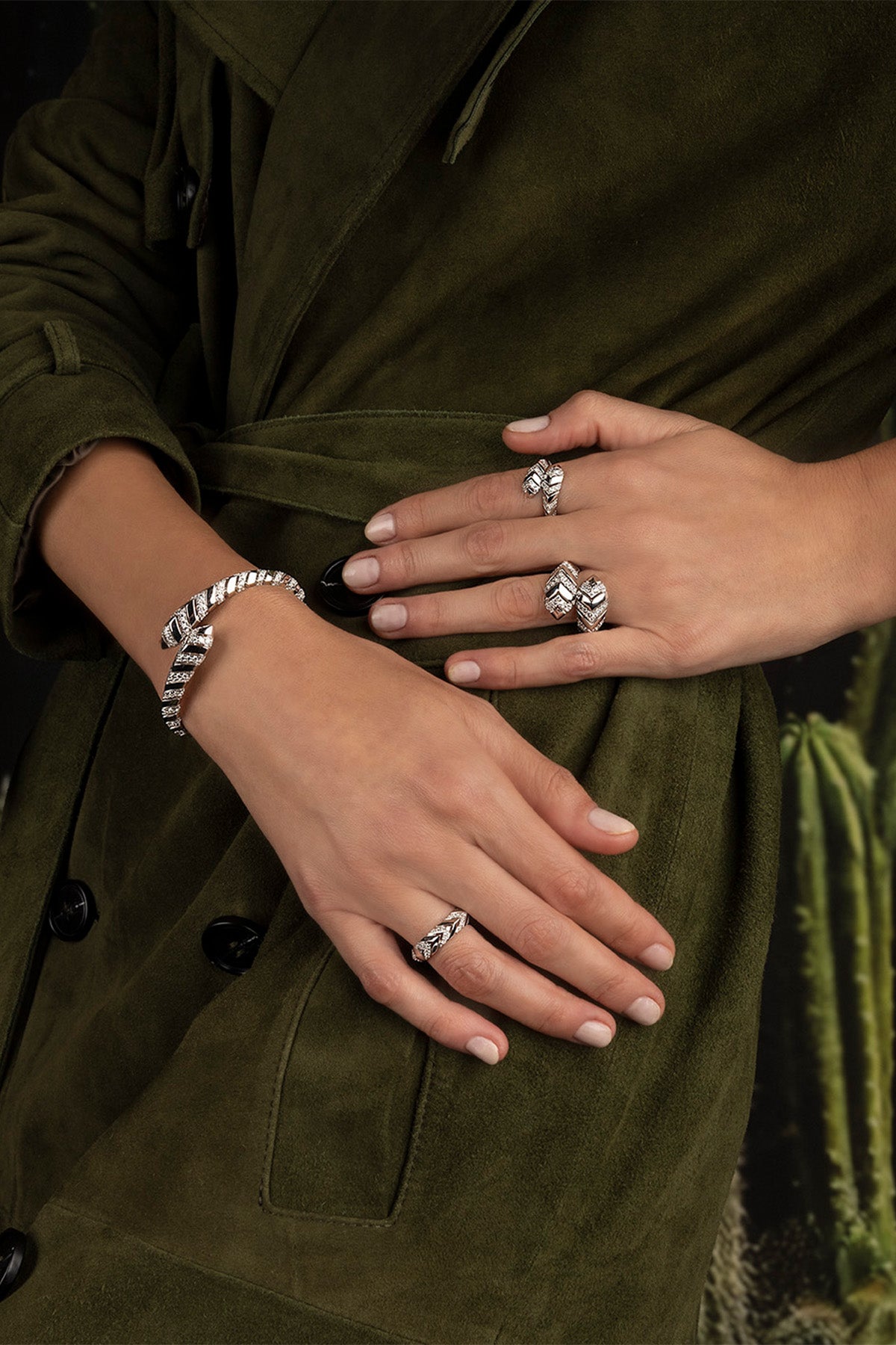 Close-up of hands wearing multiple APM MONACK KAA rings and bangles on a green fabric background