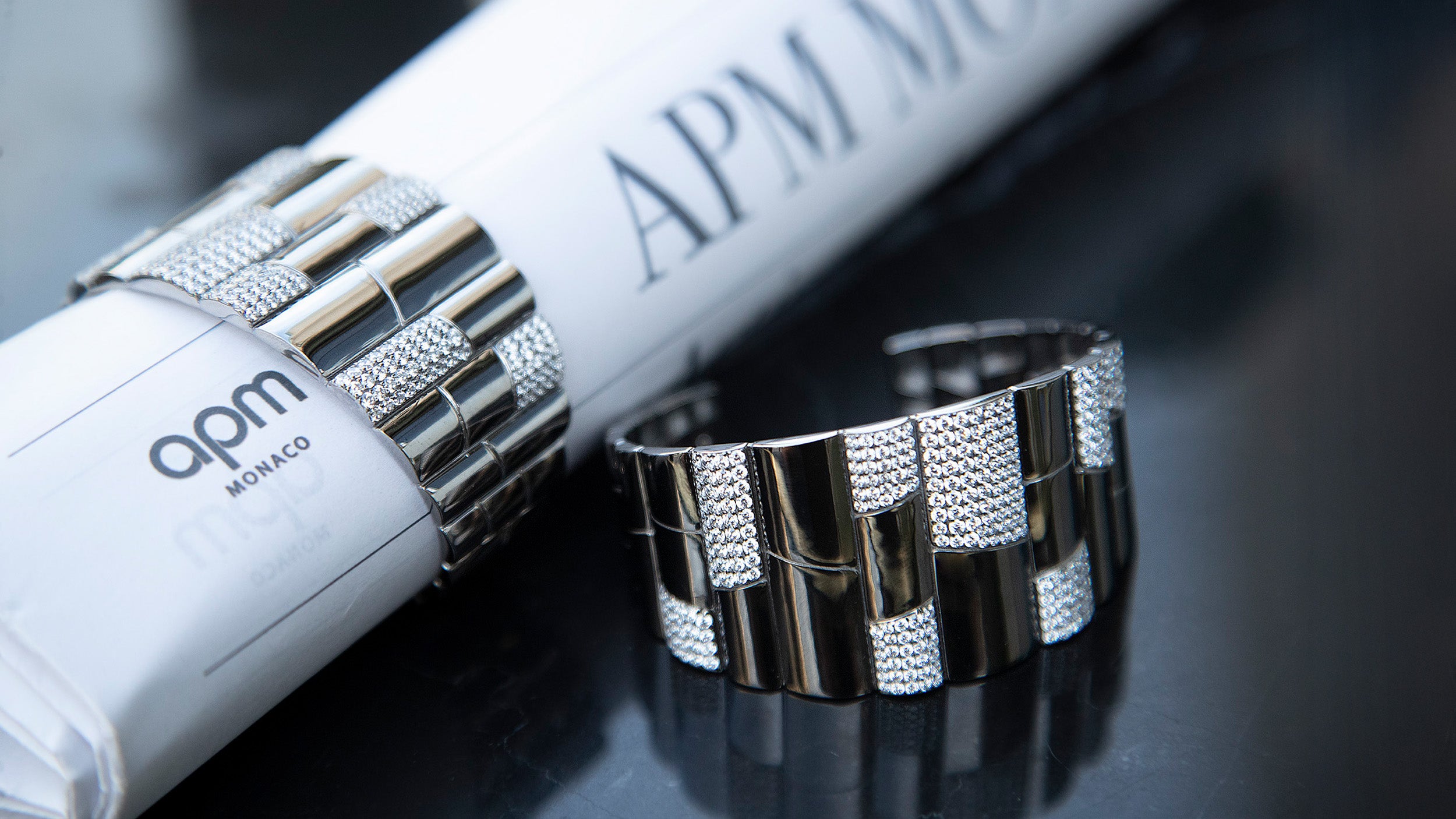 Pave silver bangle with 'apm monaco' branding on a reflective surface