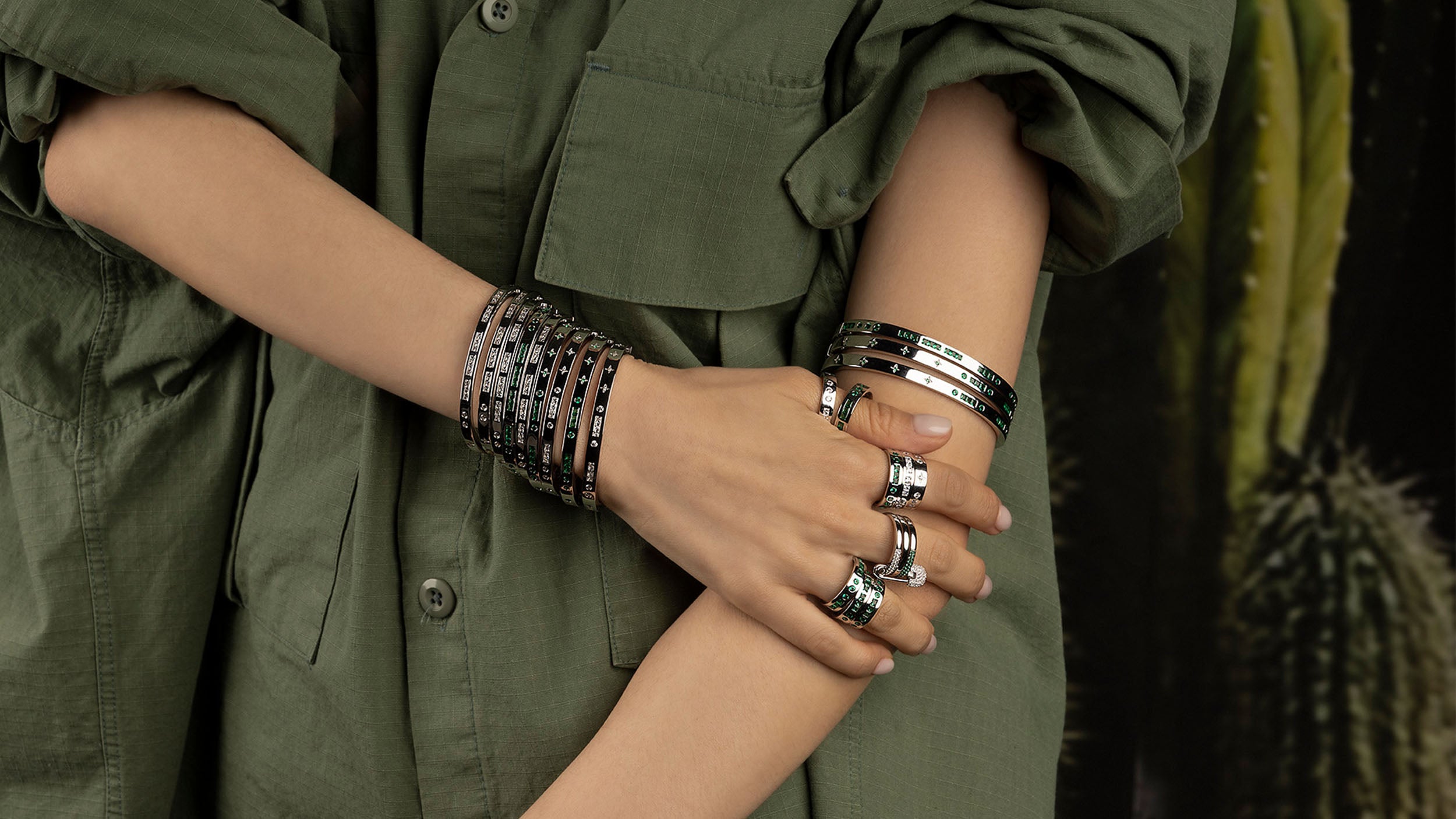 Person wearing multiple morse code bracelets and rings on a blurred green background