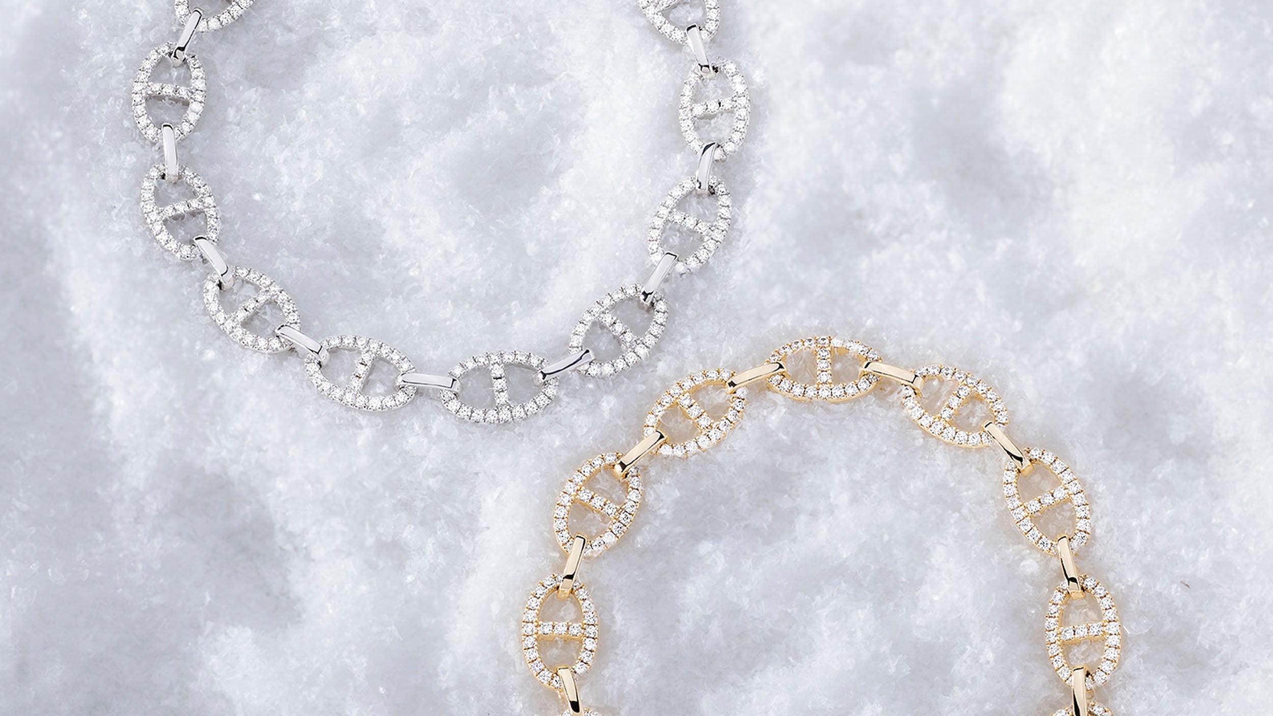 Two APM MONACO yacht club necklaces in silver and yellow gold on a textured white background