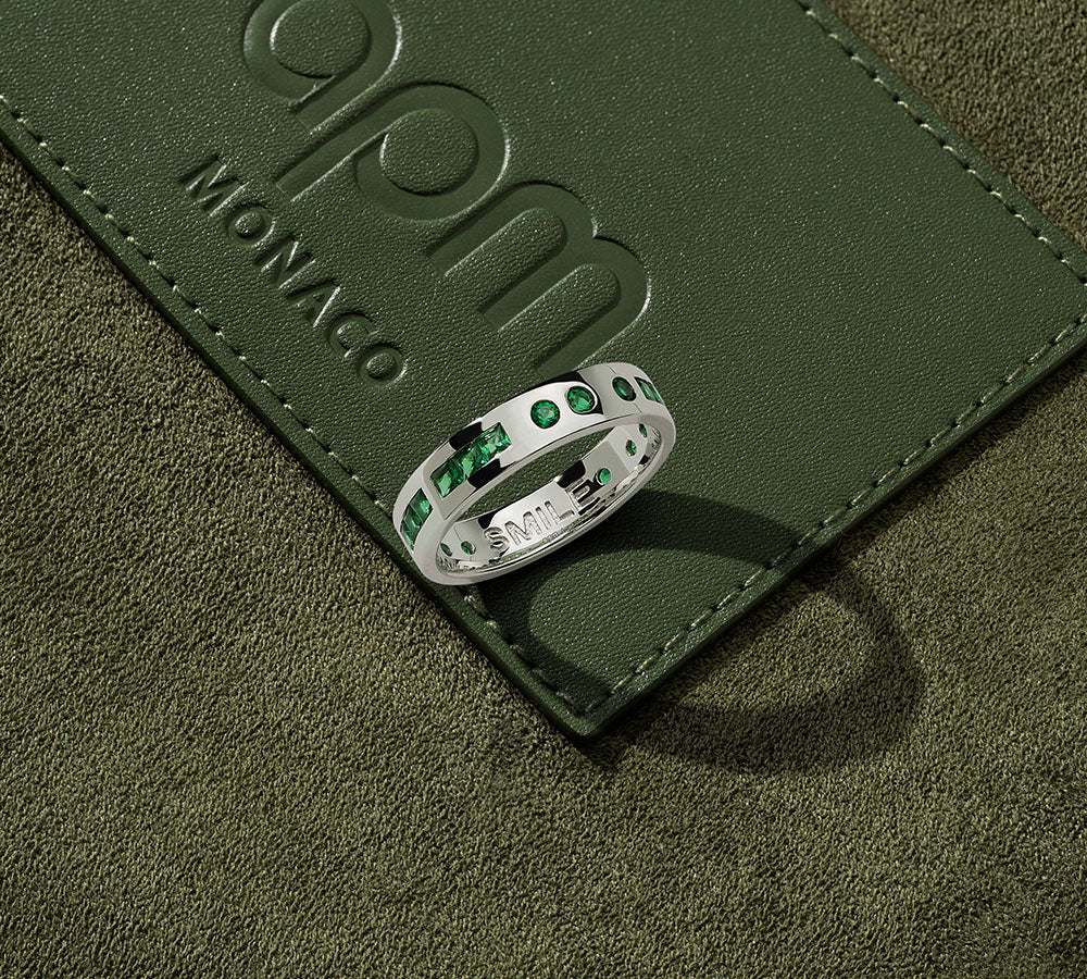 Silver morse code ring on a green leather surface with 'APM Monaco' branding.