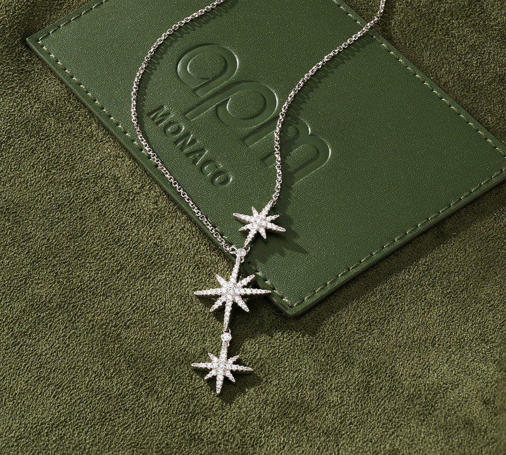 APM MONACO triple Metorites Star-shaped necklace on a green textured surface with a brand logo.