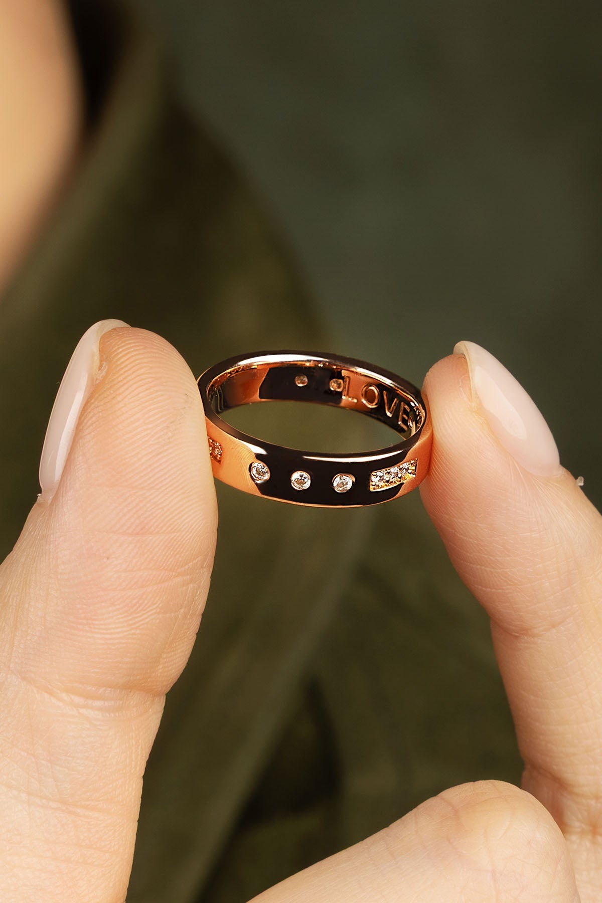Rose gold ring held between two fingers against a blurred green background