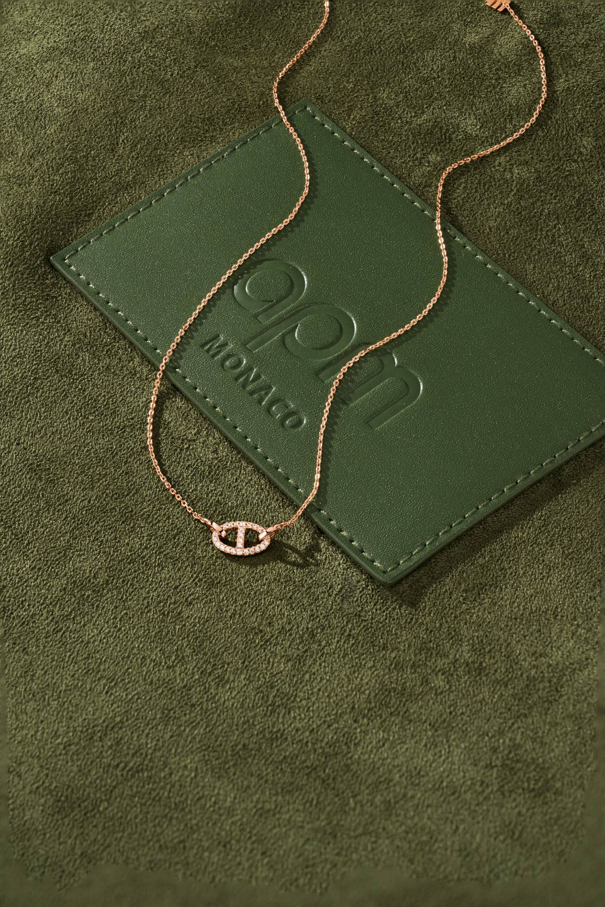 APM MONACO rose gold necklace with unique pendant on a green background