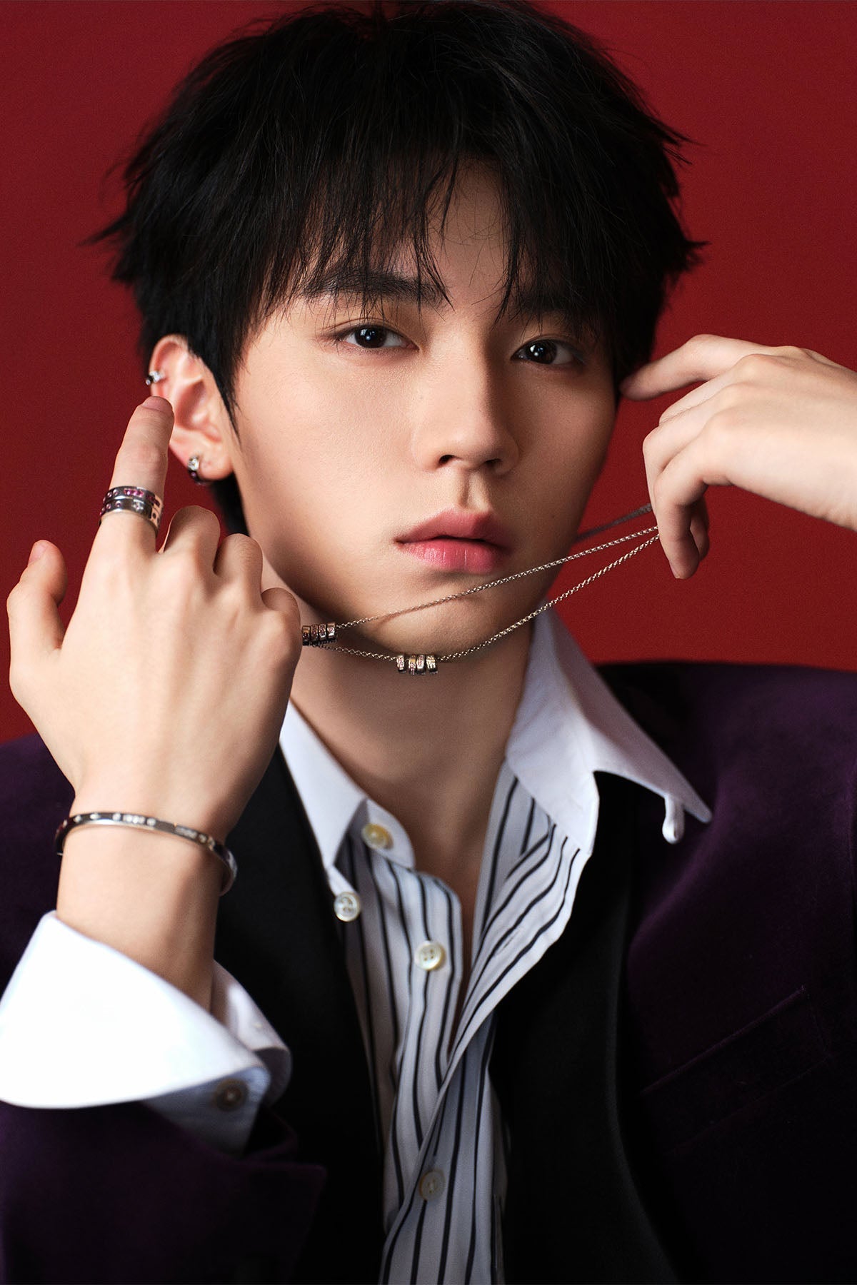 A model adjusting a necklace against a red background