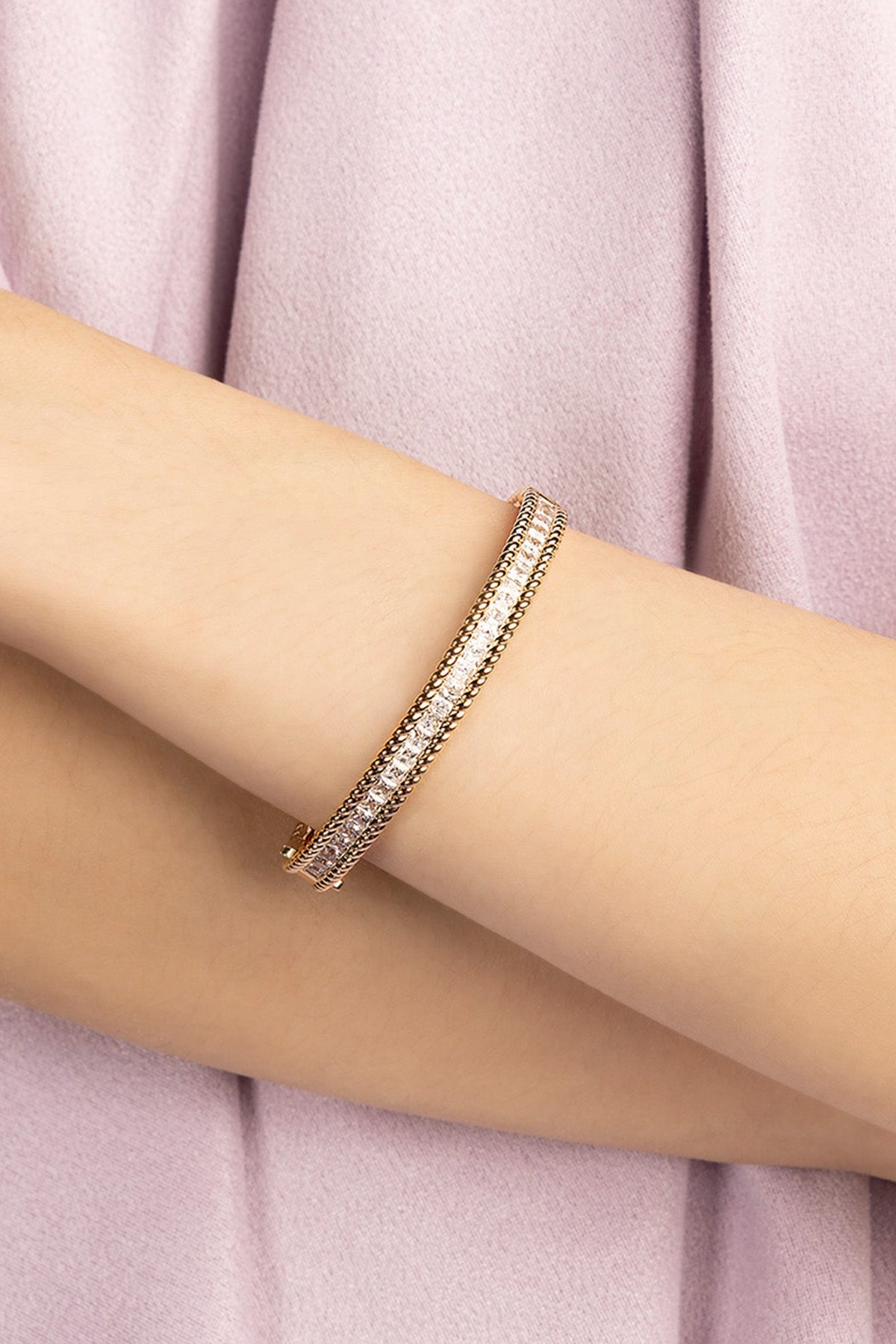 Gold bracelet on a person's wrist with a soft pink fabric background
