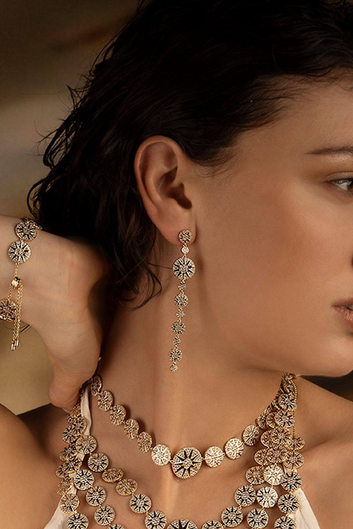 Woman wearing a gold necklace and earrings with a blurred background