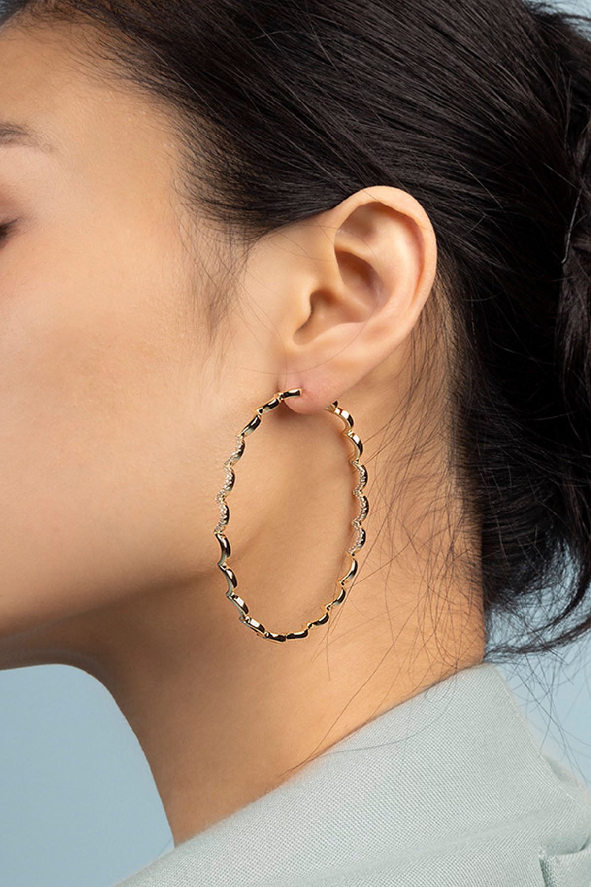 Close-up of a person wearing gold hoop earrings with a light blue background