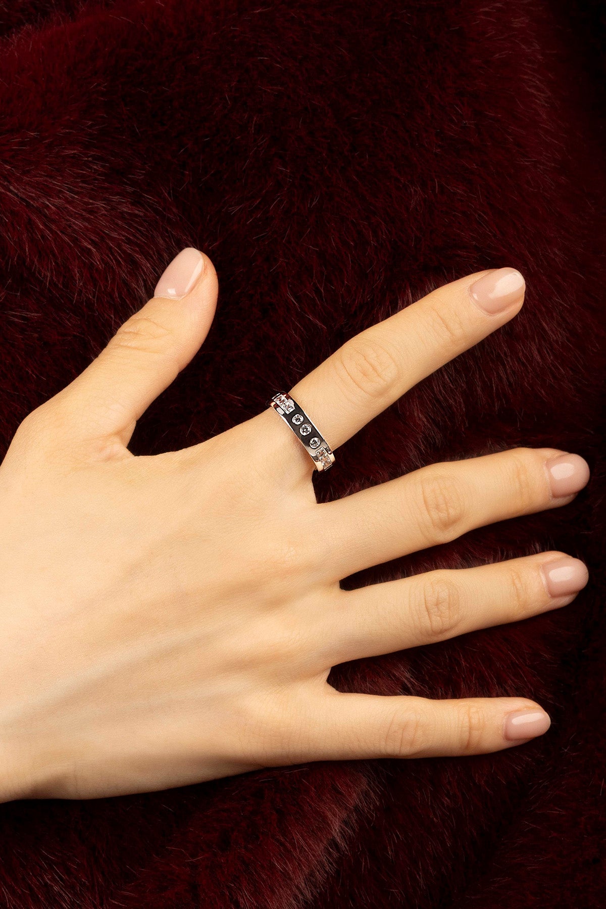 Woman wearing APM ring, quiet elegance against deep burgundy warmth.