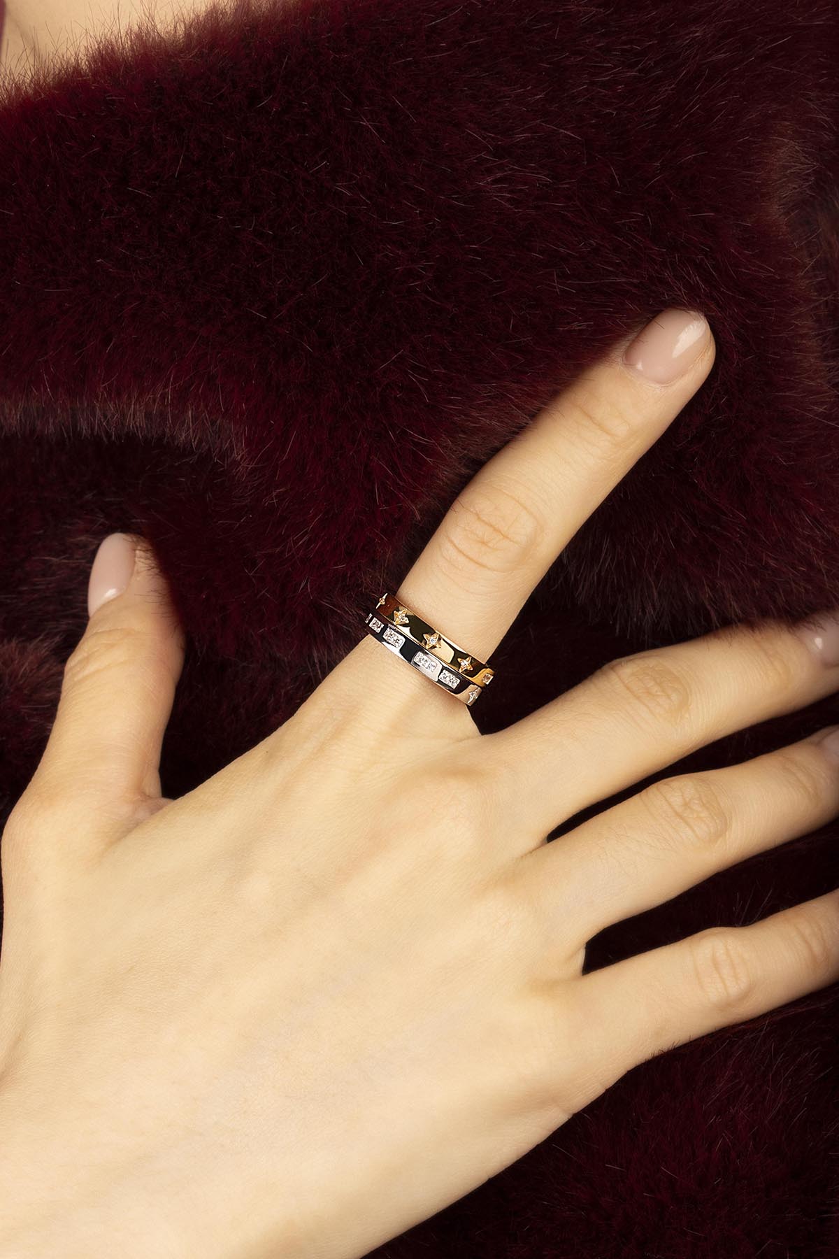 Woman wearing APM Monaco stacked rings, a whisper of stars against burgundy softness.