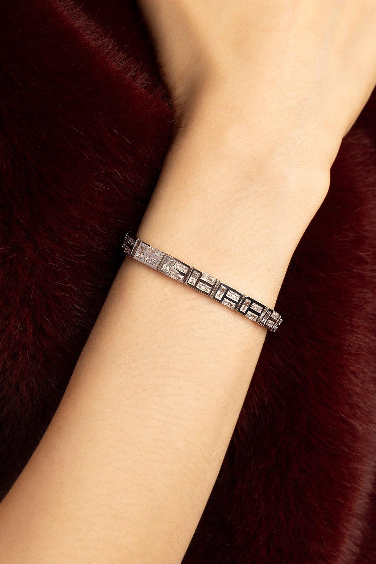 Woman wearing APM bracelet, a sleek rhodium finish glimmer against deep burgundy fur.