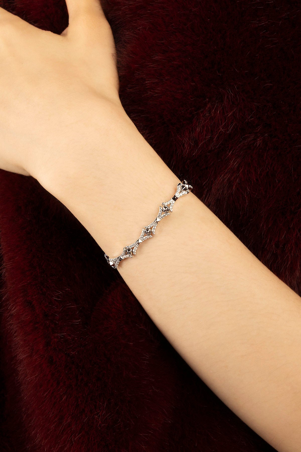 Woman wearing APM bracelet, a delicate sparkle against deep velvet elegance.