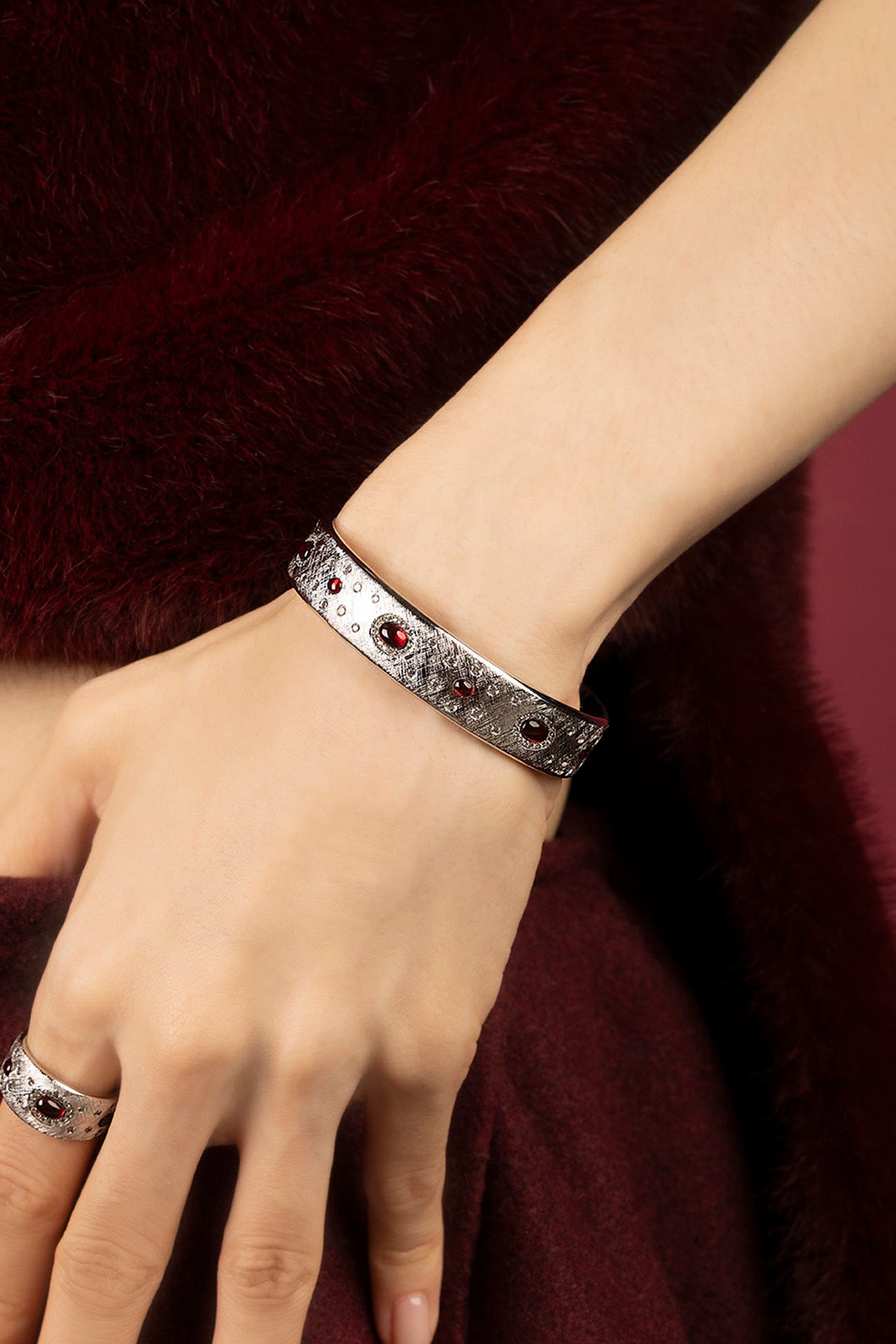 Woman wearing APM Monaco bangle, rhodium finish glowing with deep red allure.
