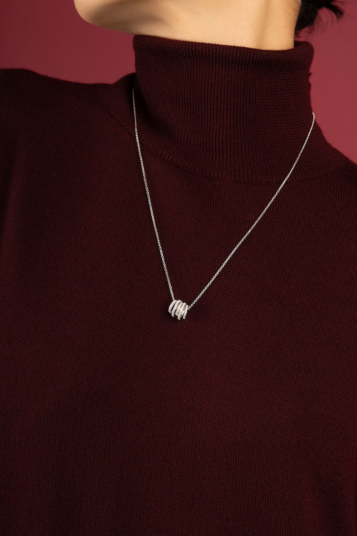 Woman wearing APM Monaco necklace, delicate rhodium finish charm resting on burgundy knit.